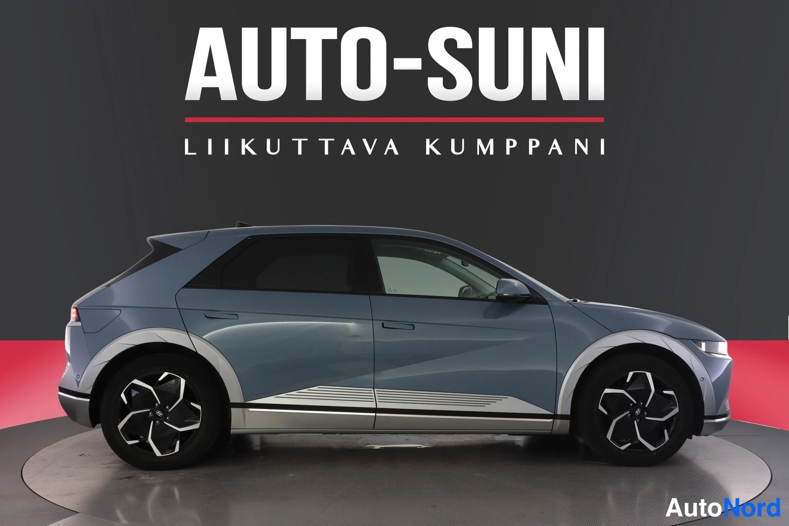 Etuviisto, nokka oikealle: Sinertävänharmaa Hyundai IONIQ 5 -sähköauto sivulta vasemmalle kääntyneenä, etupää osittain näkyvissä.