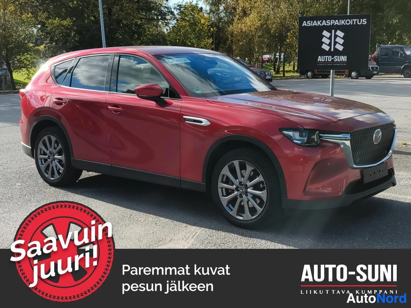 Etuviisto, nokka oikealle: Punainen Mazda CX-60 etuviistosta oikealta kuvattuna parkkipaikalla, taustalla Auto-Sunin asiakaspaikoitus-kyltti.