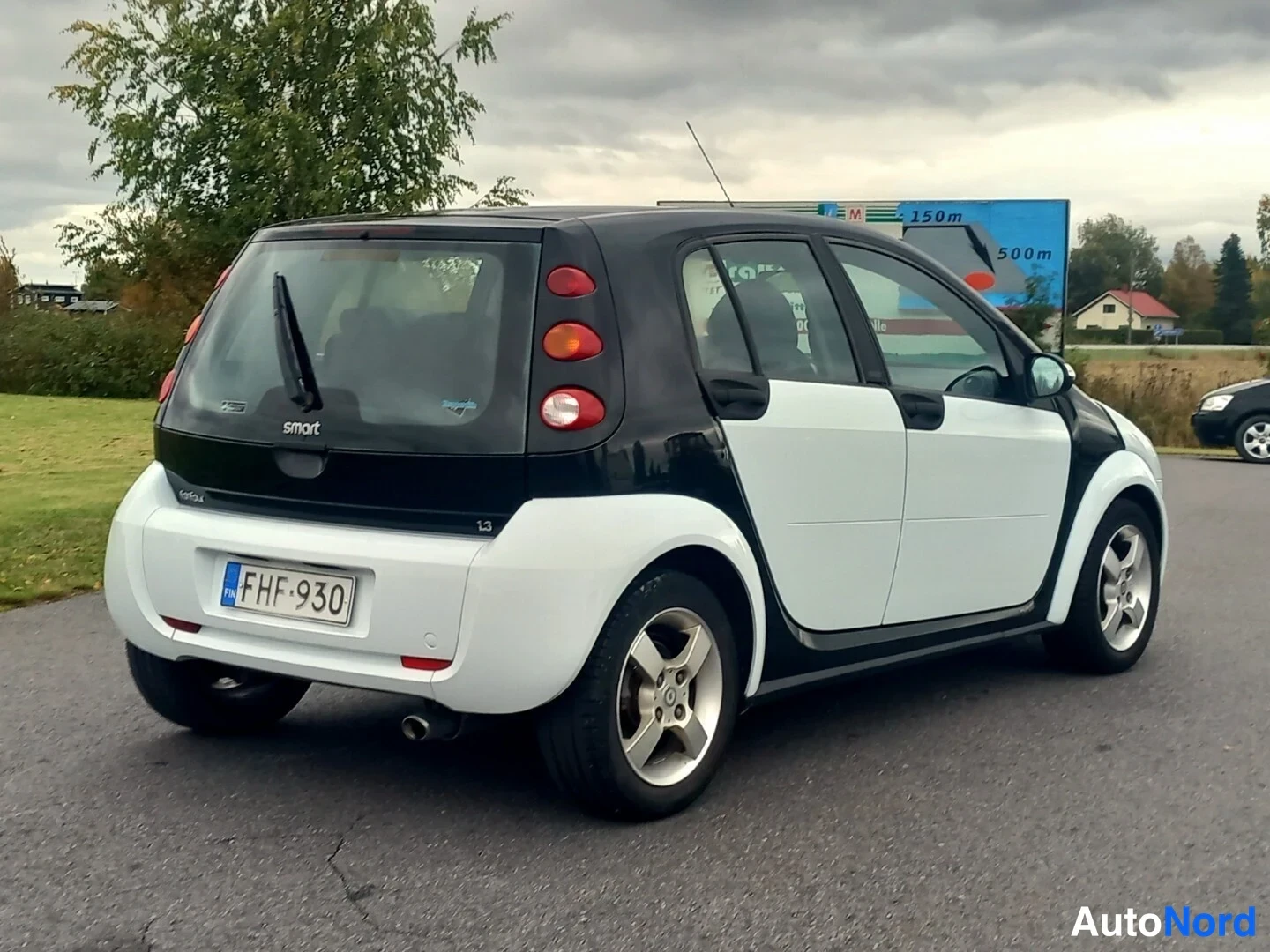 Takaviisto: Valkoinen ja musta Smart Forfour -henkilöauto takaviistosta vasemmalta kuvattuna, rekisterikilpi.