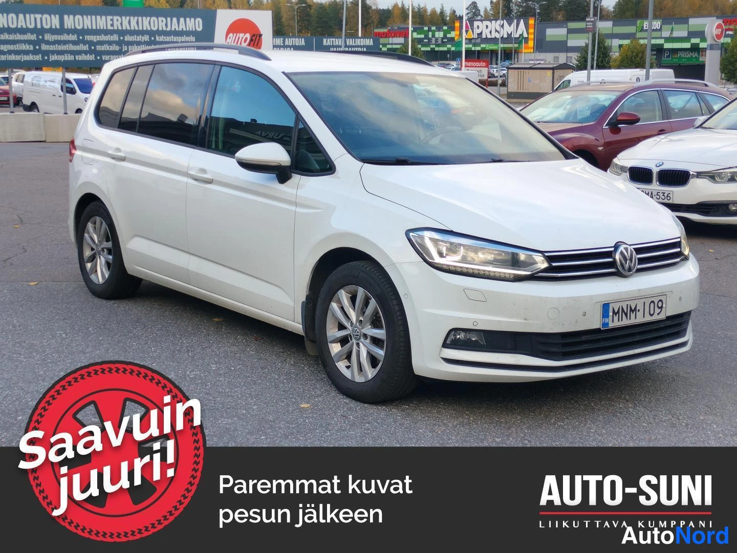 Etuviisto, nokka oikealle: Valkoinen Volkswagen Touran etukulmasta, rekisteritunnus, autopaikalla kauppakeskuksen edustalla.