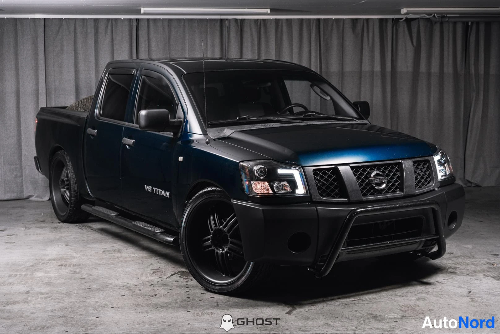 Etuviisto, nokka oikealle: Tummansininen Nissan Titan -haustyylikuorma-auto kuvattu kolmasosaedusta oikealta, tummat vanteet ja musta etupuskurikaari.