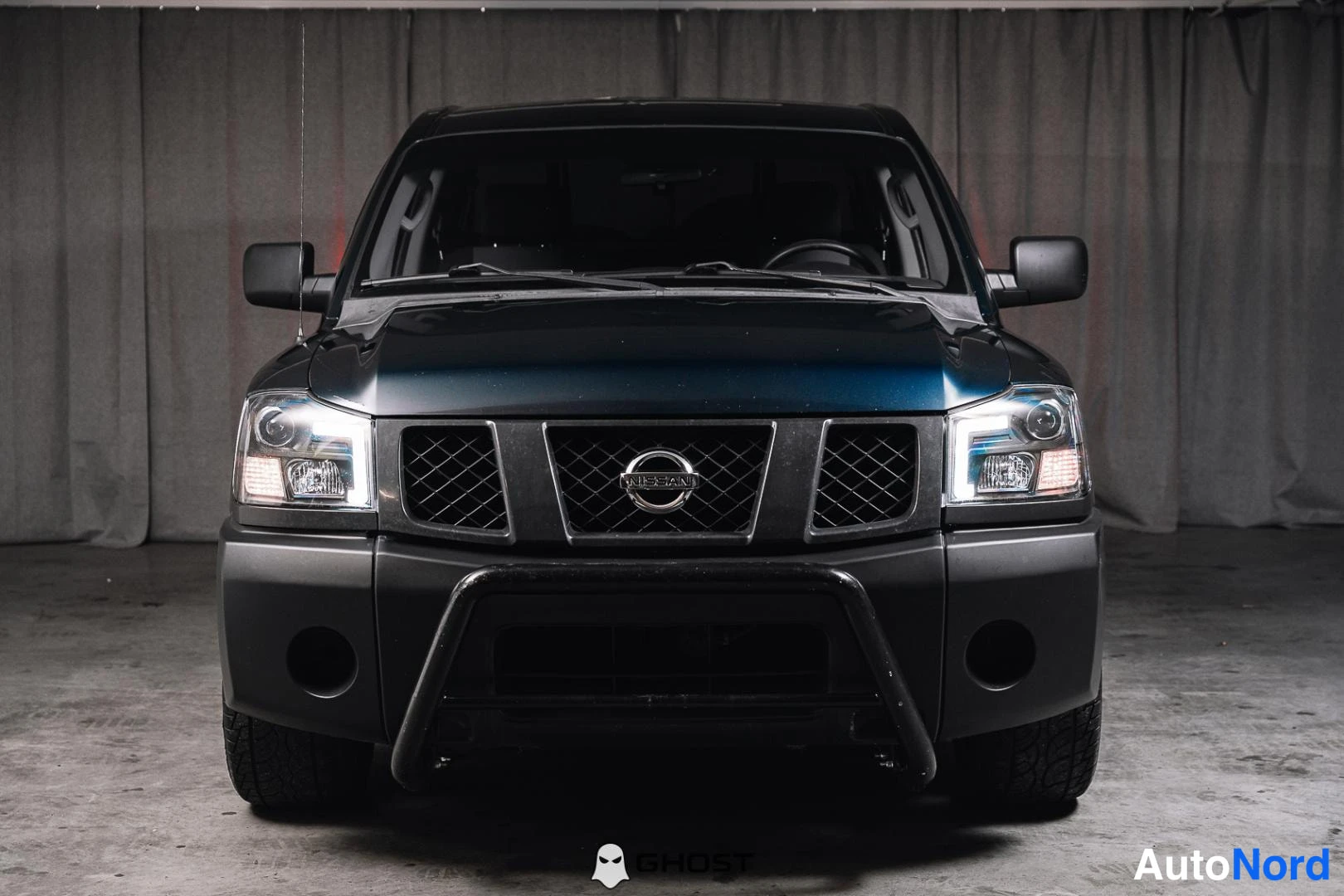Edestä: Tummansininen Nissan Titan suoraan edestä kuvattuna, musta etupuskuri ja kaaripuskuri, konekoppitunnus Nissan.