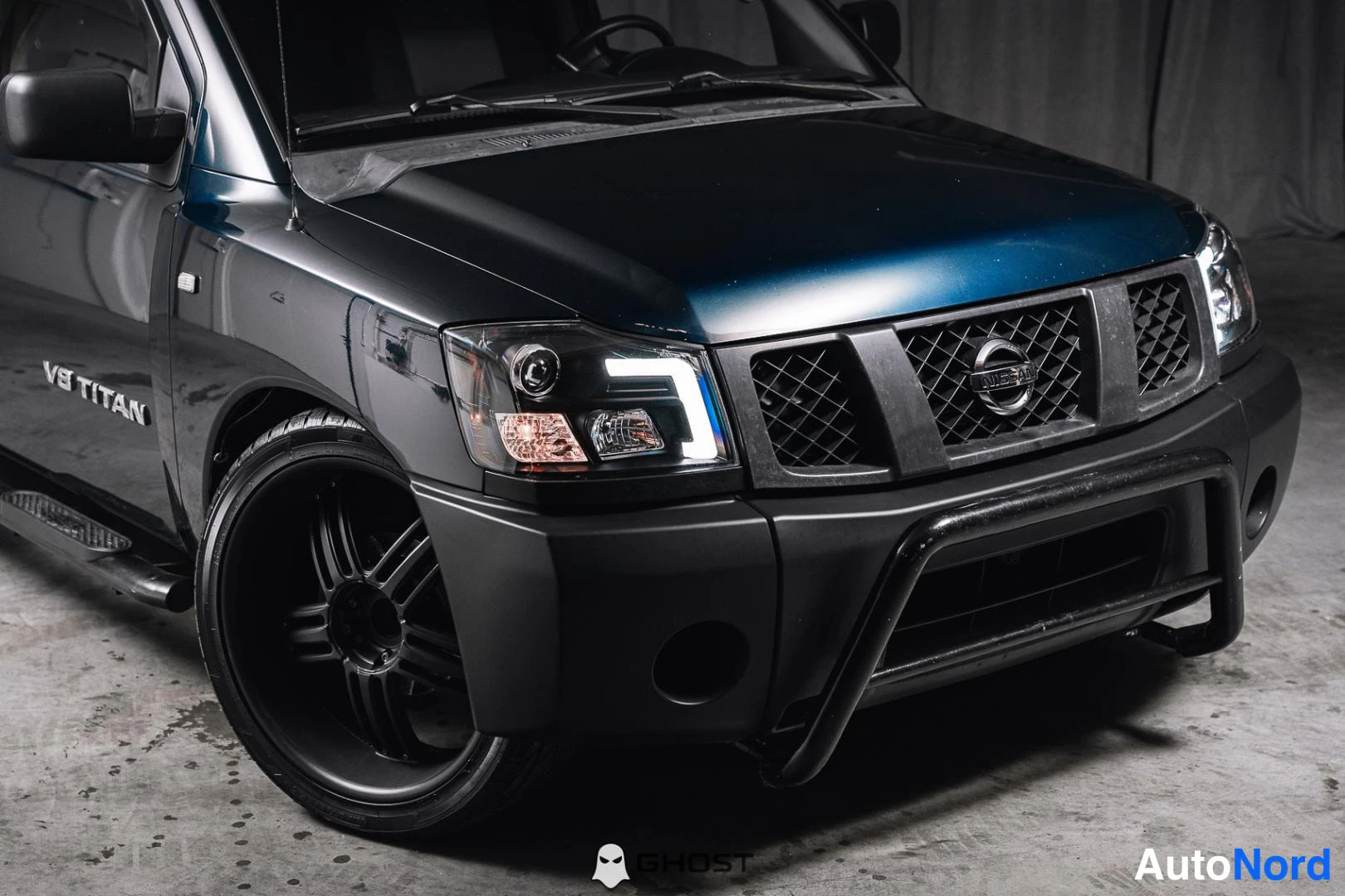 Etuviisto, nokka oikealle: Tummansinisen Nissan Titanin etukolmannes oikealta: V8 TITAN -teksti ovessa, mustat vanteet ja etupuskurikaari.