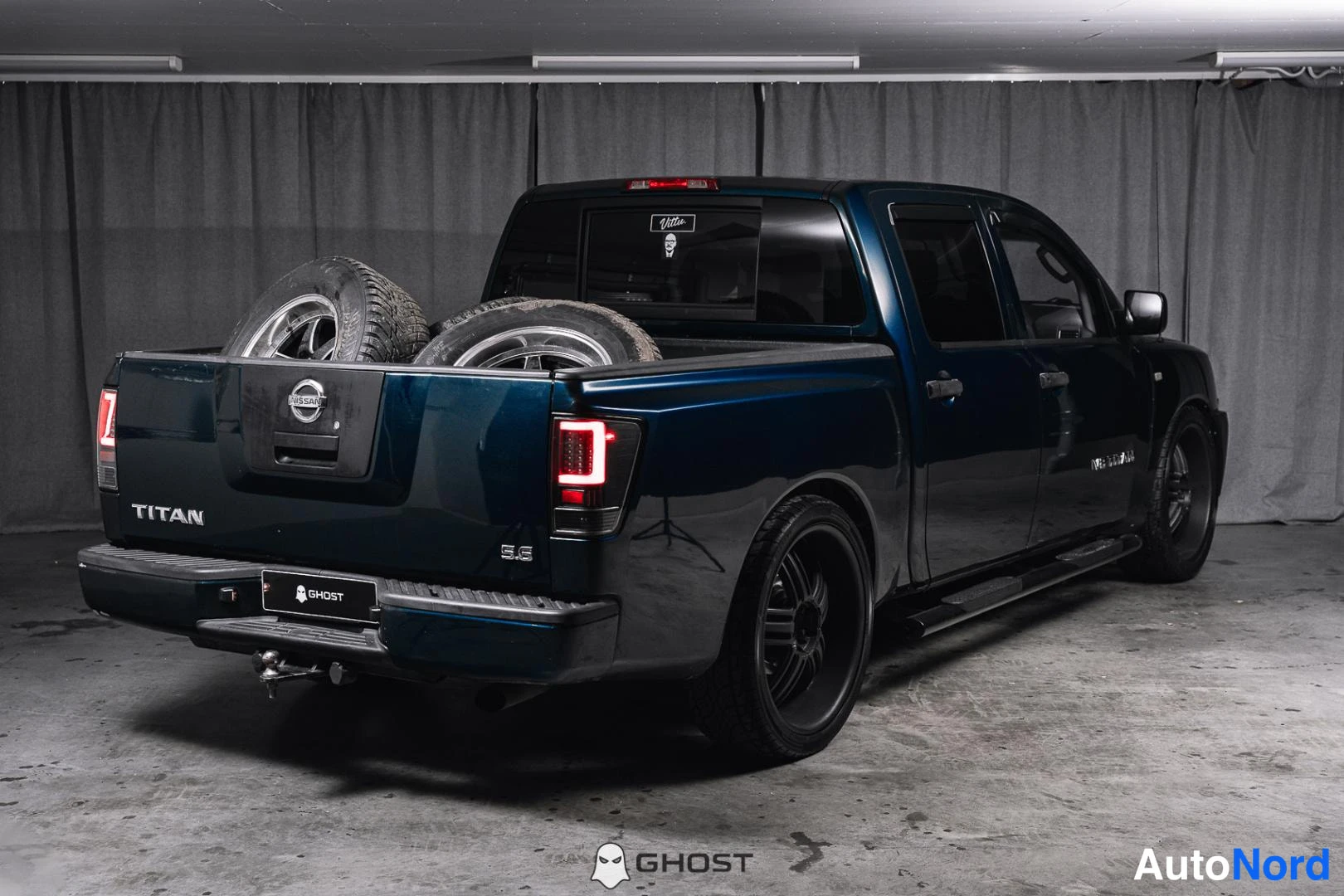 Takaviisto: Tummansinisen Nissan Titan -lava-auton takakulma, lavassa kolme vaihtorengasta.