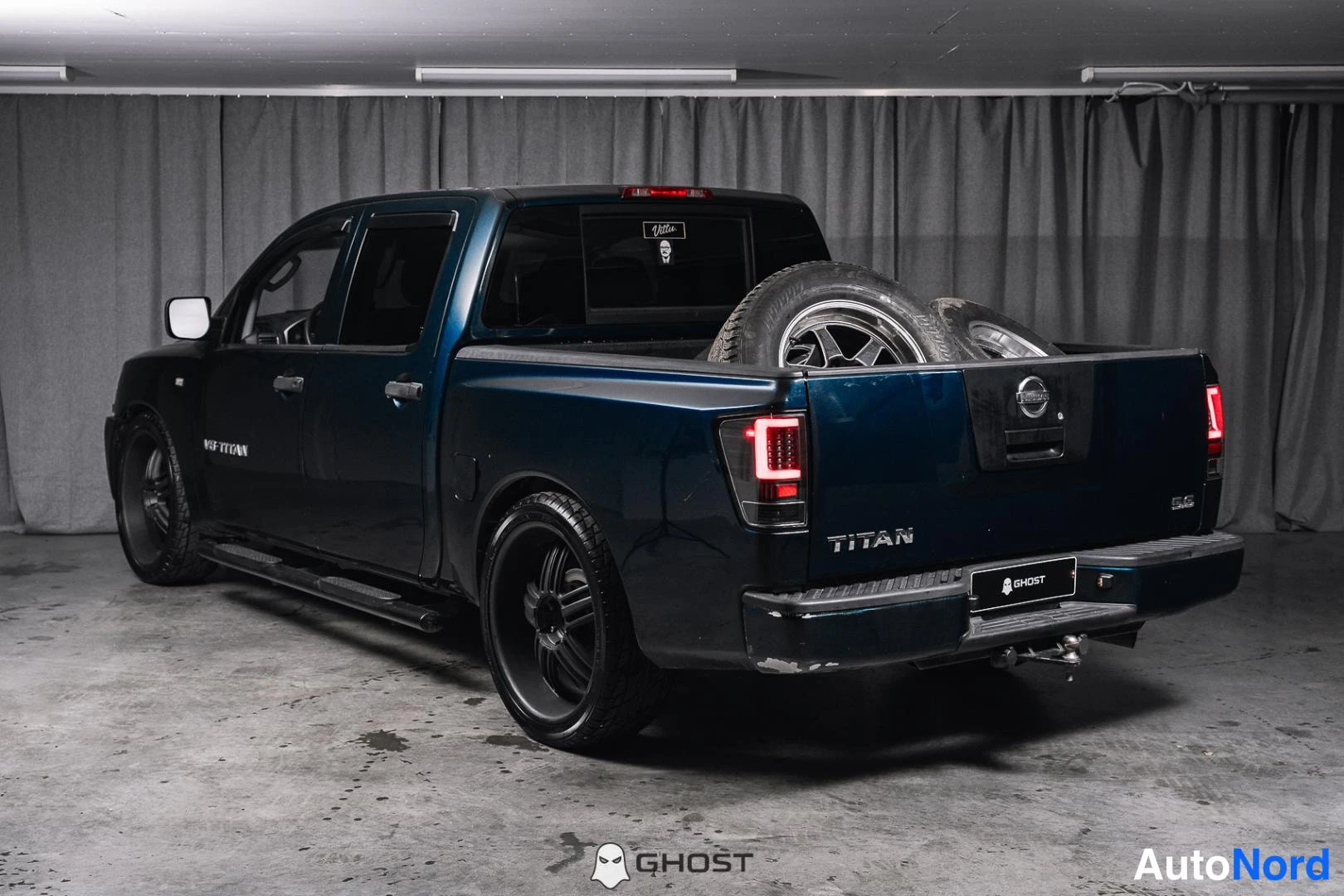 Takaviisto: Tummansininen Nissan Titan -lava-auto takakulmasta, lavassa vaihtorenkaita, TITAN-teksti takaluukussa.