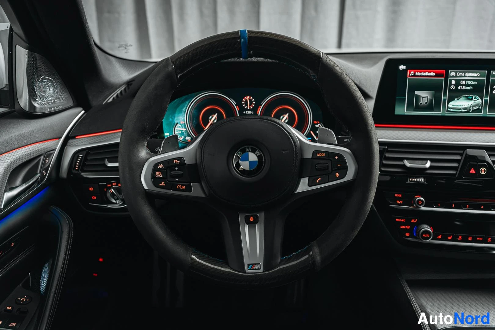 Etuviisto, nokka vasemmalle: BMW-ohjauspyörän lähikuva: M-merkki, monitoiminapit ja digitaalinen mittaristo punaisine valoineen.