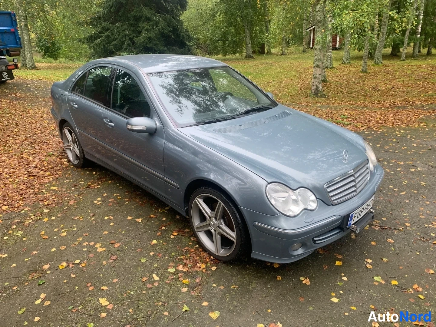 Etuviisto, nokka oikealle: Harmaa Mercedes-Benz sedan etuosa oikealta neljännesnäkymästä, koko auto näkyvissä, rekisteritunnus.