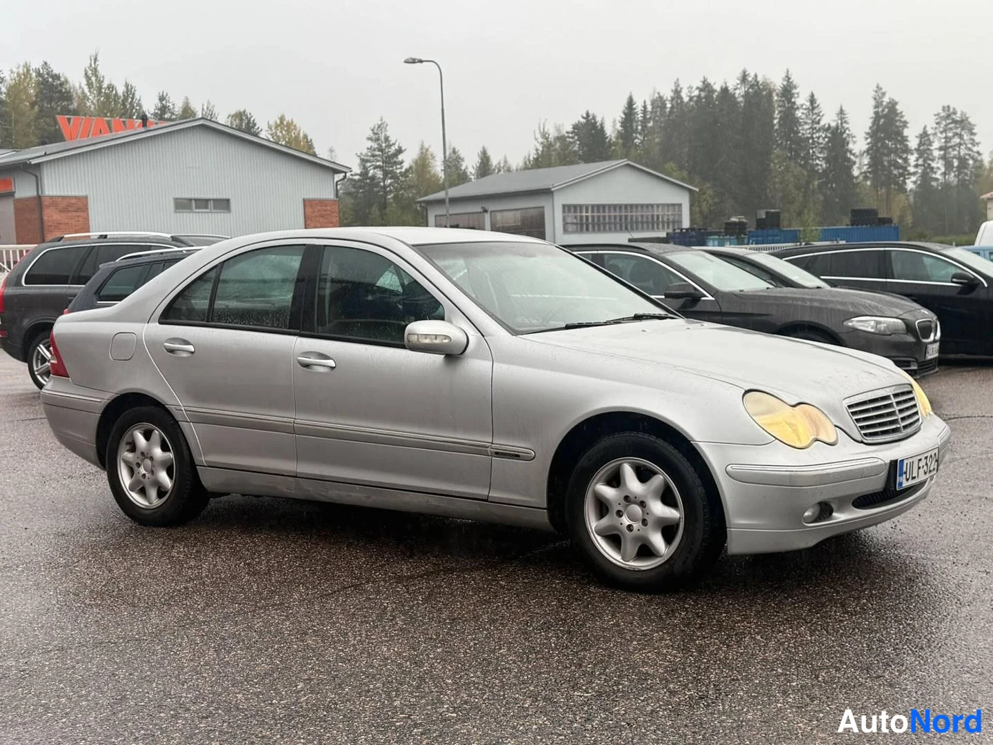 Etuviisto, nokka oikealle: Hopeanharmaa Mercedes-Benz C-sarjan sedan edestä oikealta kolmantenaäkuvana, rekisteritunnus.