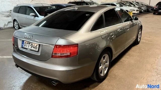 Takaviisto: Hopeanharmaa Audi A6 -sedan kuvattu takakulmasta: takavalo, rekisteritunnus ja auton oikean puolen ovet sekä pyörät näkyvät.