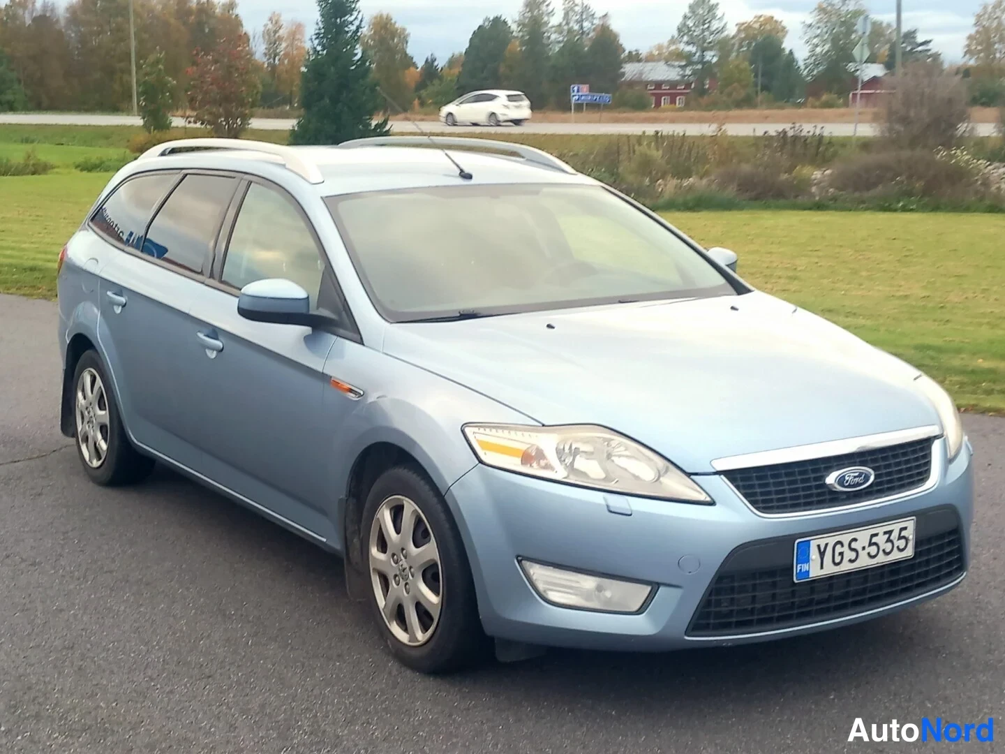 Etuviisto, nokka oikealle: Vaaleansininen Ford Mondeo -farmari kolmannelta paaleelta, keula oikealla. Kattokaiteet, etuvilkut ja rekisterikilpi näkyvät.