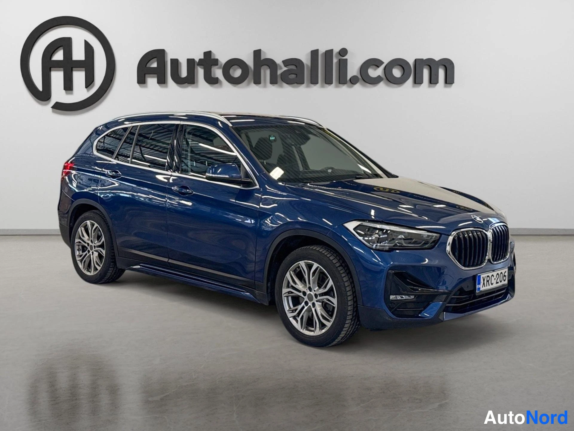 Etuviisto, nokka oikealle: Tummansininen BMW X1 kulmakuvassa edestä oikealta; etusäleikkö, ajovalot ja kylki näkyvissä, rekisterikilpi lukee.