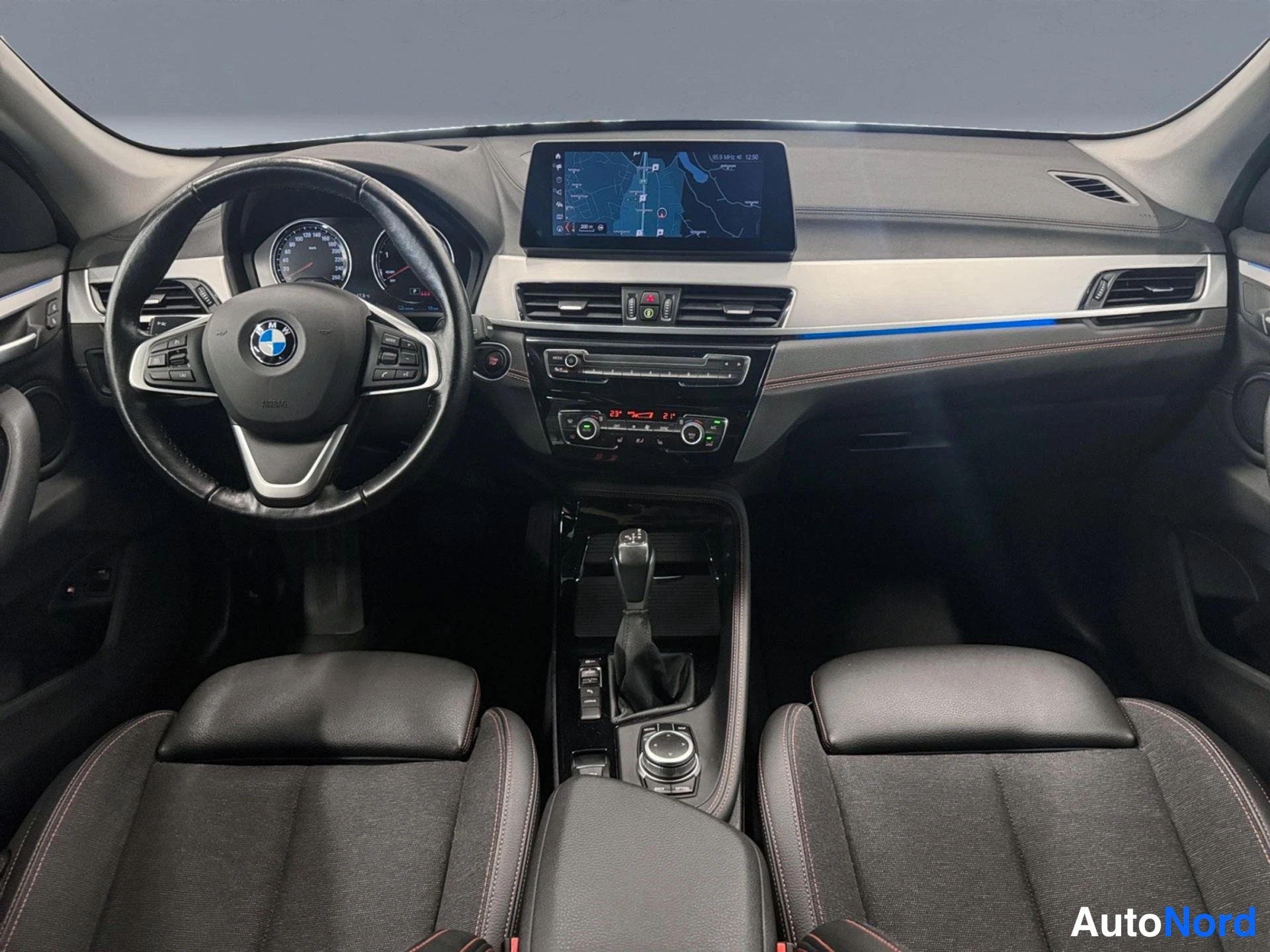Muu: Sisätilakuva: BMW-tunnuksellinen ohjauspyörä, karttaa näyttävä keskinäyttö kojelaudassa, automaattivaihteen valitsin keskikonsolissa ja kaksi etuistuinta tummal
