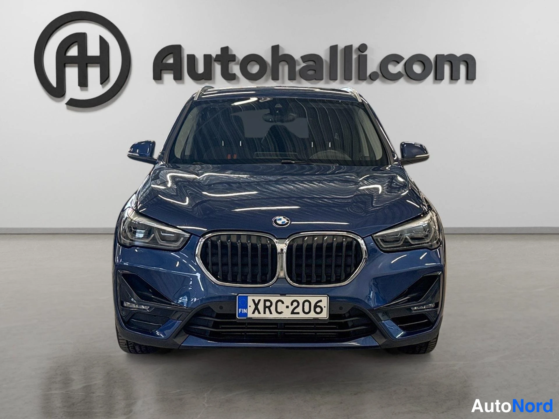 Edestä: Tummansininen BMW X1 suoraan edestä kuvattuna; munuaissäleikkö, ajovalot ja rekisterikilpi näkyvissä.