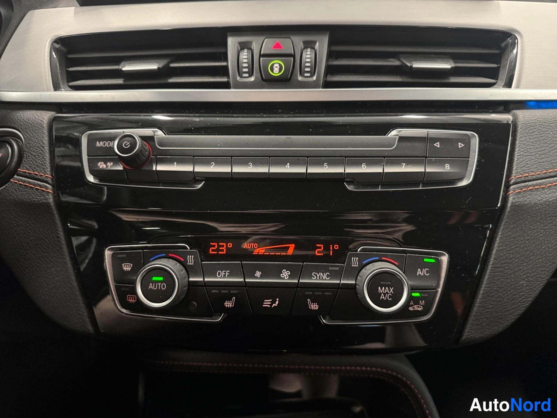 Yksityiskohta: Keskikonsolin kaksialueinen automaatti-ilmastointipaneeli: näytöillä 23° ja 21°, painikkeet AUTO, OFF, SYNC, A/C ja MAX A/C, sekä kahdeksan radion esiasetusnapp