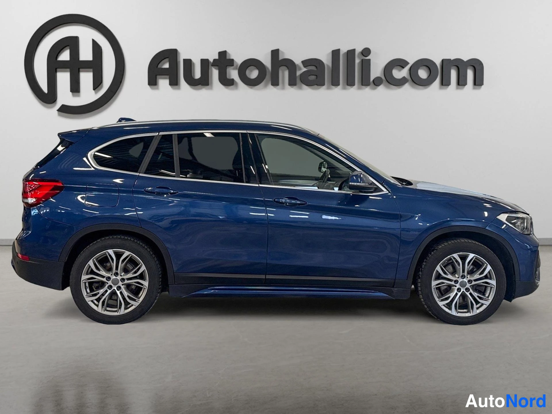 Etuviisto, nokka oikealle: Tummansininen BMW X1 kuvattuna etukulmasta, keula oikealla; auton kylki, etuvalo ja hopeanväriset kevytmetallivanteet näkyvät.
