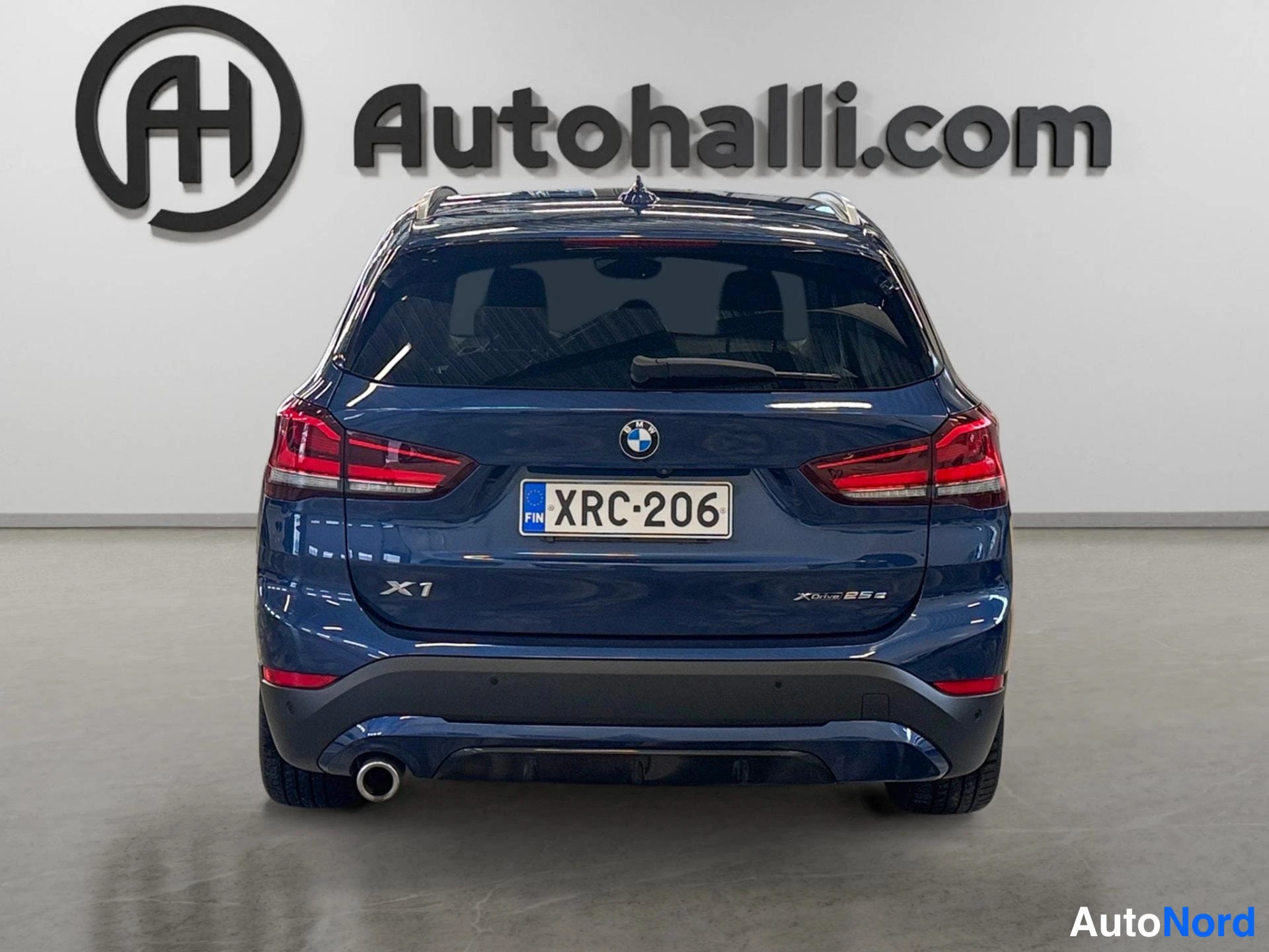 Takaa: Takaapäin kuvattu tummansininen BMW X1; rekisterikilpi, BMW-emblemi sekä X1- ja xDrive 25e -merkit takaluukussa, pakoputki vasemmalla.