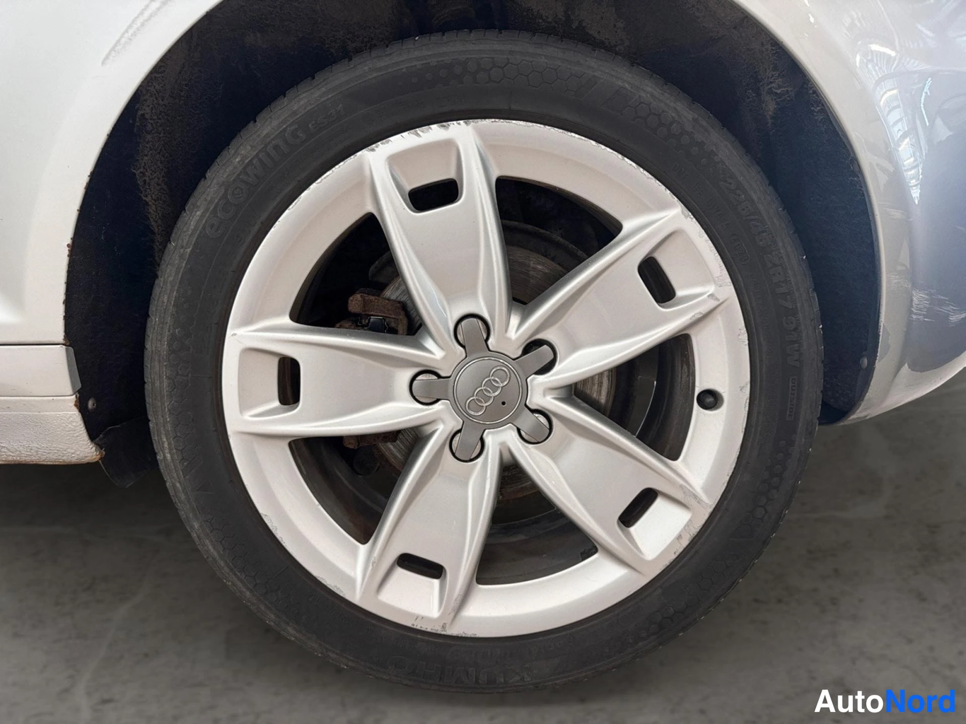Yksityiskohta: Lähikuva auton pyörästä: hopeinen viisipuolainen vakiovanne Audi-tunnuksella ja musta Ecowing-renkaaseen painettu teksti näkyvissä.