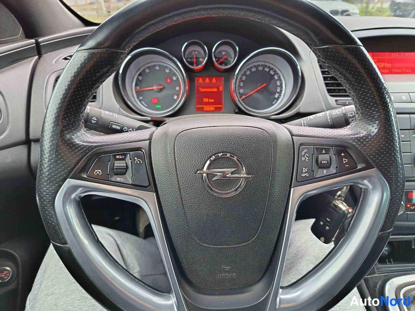 Yksityiskohta: Close-up of steering wheel with Opel logo multifunction buttons key in ignition and instrument cluster behind