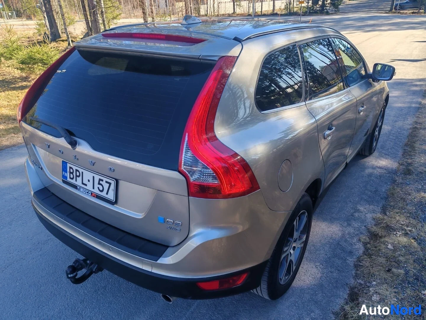 Takaviisto: Auton perä ja oikea kylki viistosti kuvattuna: takaluukussa VOLVO- ja D5 AWD -tekstit, rekisterikilpi sekä vetokoukku takapuskurissa. Korin väri on beige.
