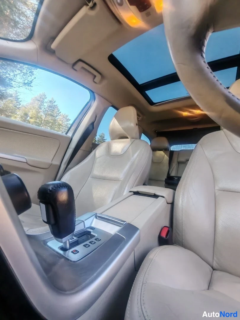 Sivulta: Sisäkuva etupenkeiltä taakse: panoraamakatto lasipaneeleilla, beige nahkaverhous ja automaattivaihteen valitsin keskikonsolissa.