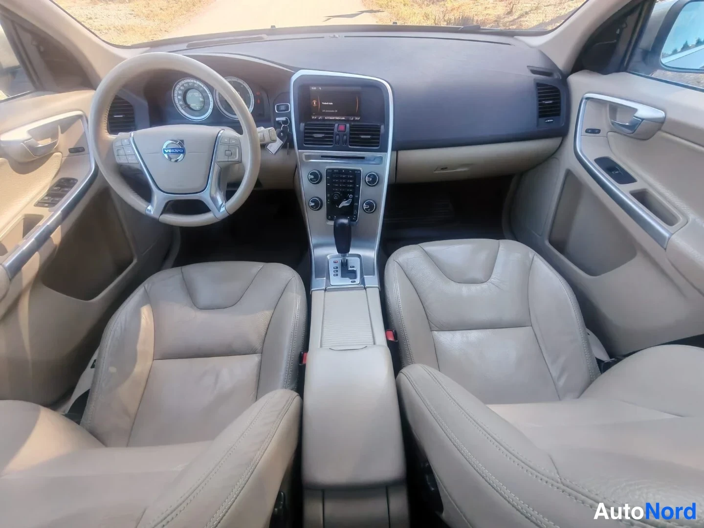 Muu: Auton sisätilat ohjaamosta taakse: beige nahkapenkit, Volvo-ohjauspyörä, keskikonsoli automaattivaihtoeikeudella ja infotainment-näytöllä.