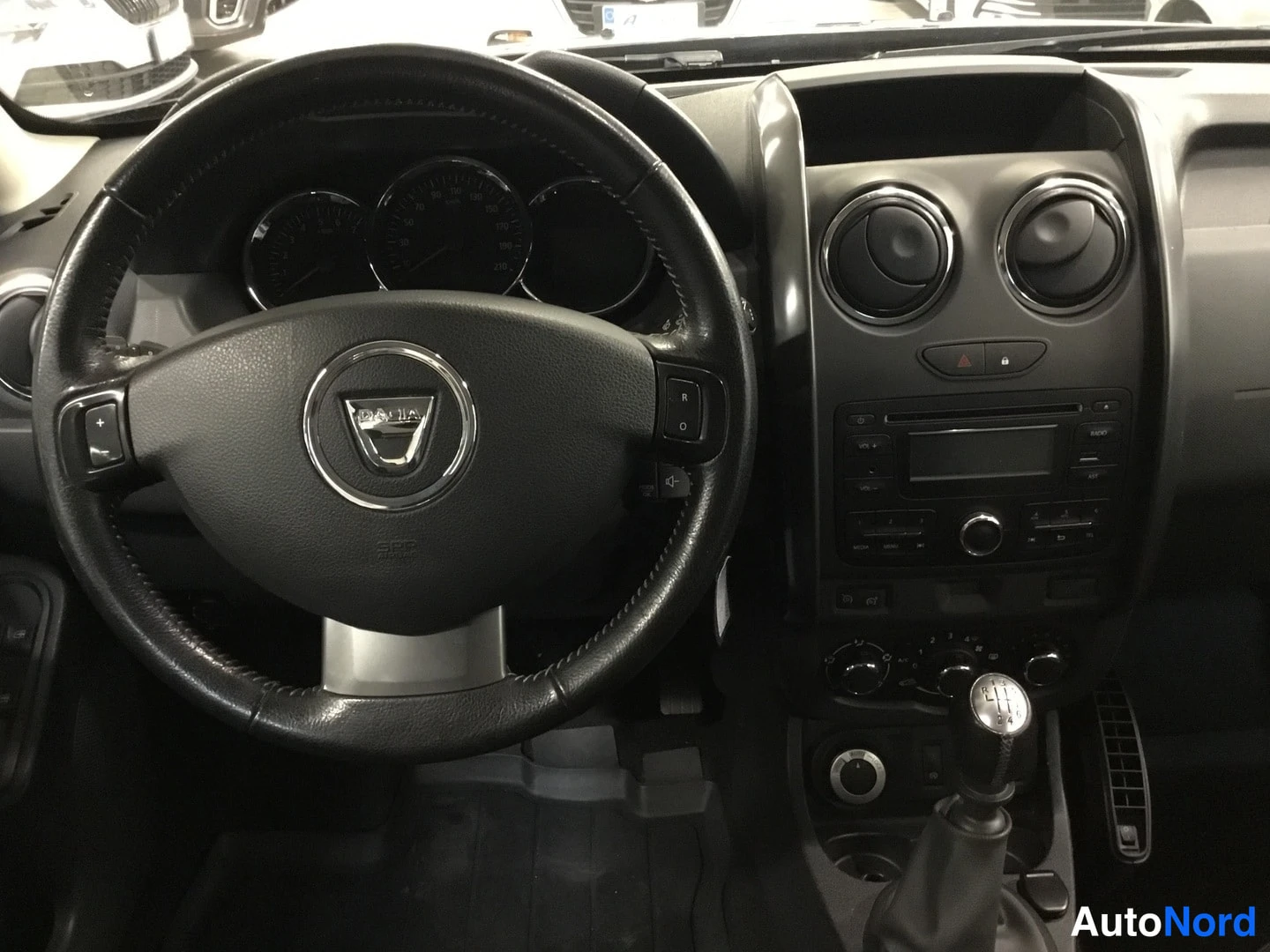 Muu: Dacia Dusterin ohjaamo: Dacia-logollinen ohjauspyörä, mittaristo, pyöreät ilmastointisuuttimet, radio ja vaihteenlevytys.