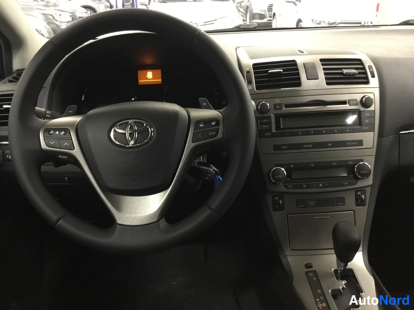 Yksityiskohta: Ohjaamon etunäkymä: Toyotan ratin napit, keskiö konsoli radion ja automaattivaihteiston valitsimella (P R N D).