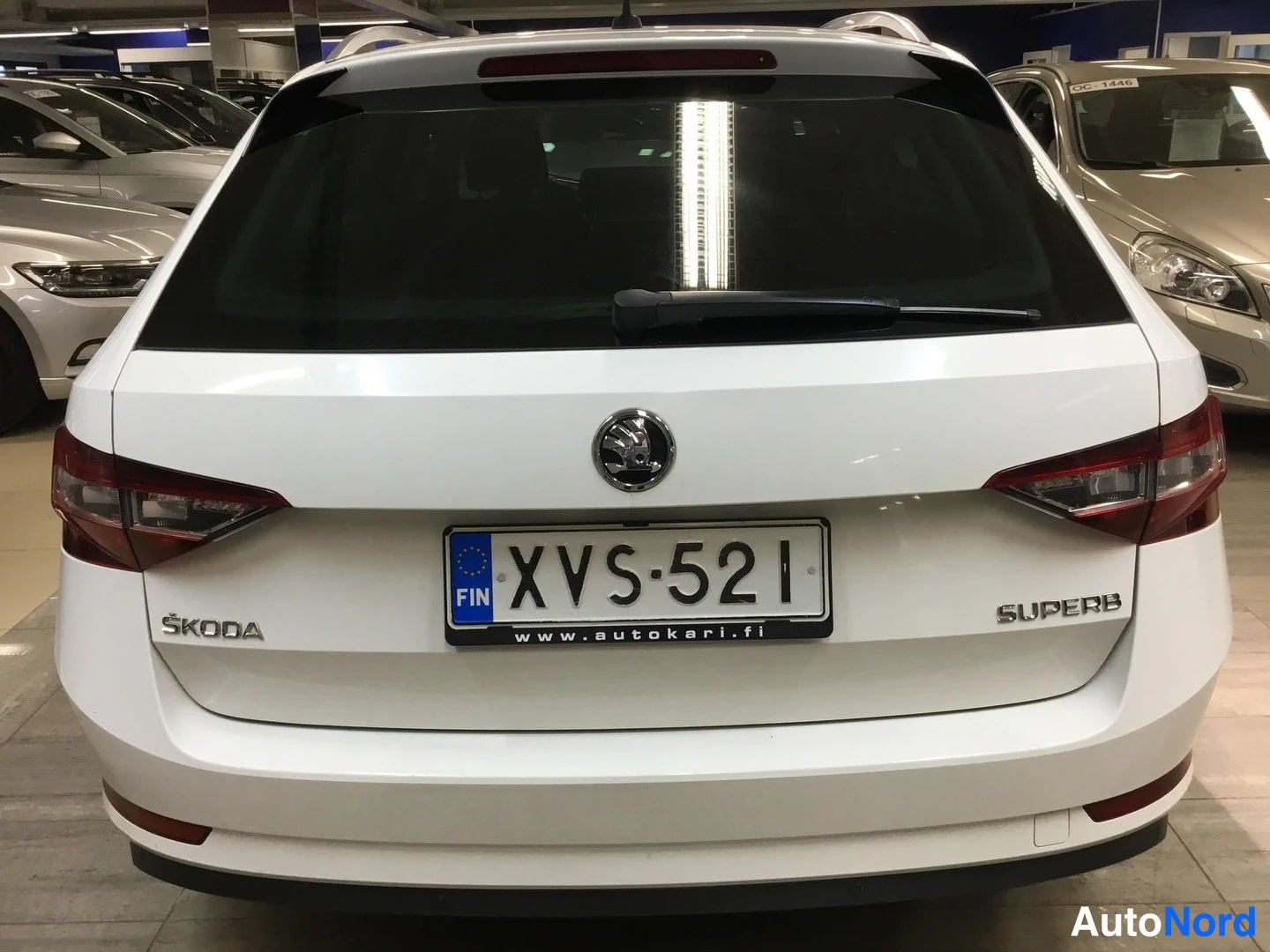Takaa: Valkoisen Skoda Superbin takaosa suoraan takaa, SKODA- ja SUPERB-merkinnät, rekisterikilpi ja takavaloat näkyvät.