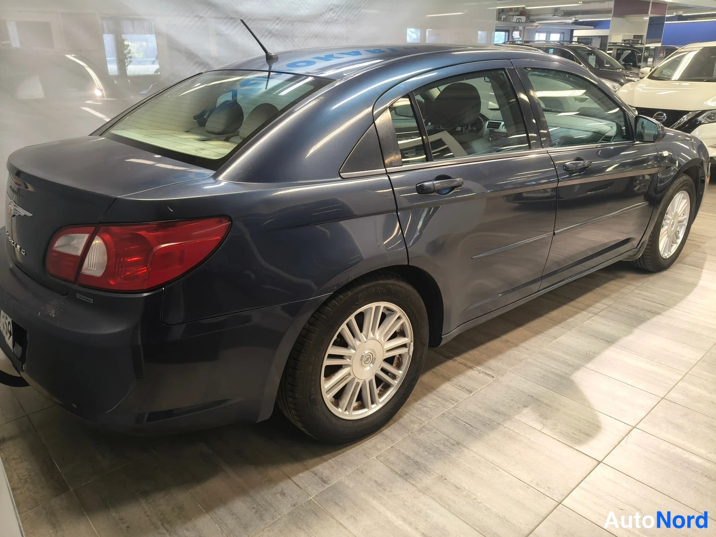 Takaviisto: Chrysler Sebring -sedanin takaosa ja oikea sivuprofiili kolmen neljäsosan kulmasta; tummansininen koriväri, punaiset takavalot, kromattu Chrysler-merkki, hopeis