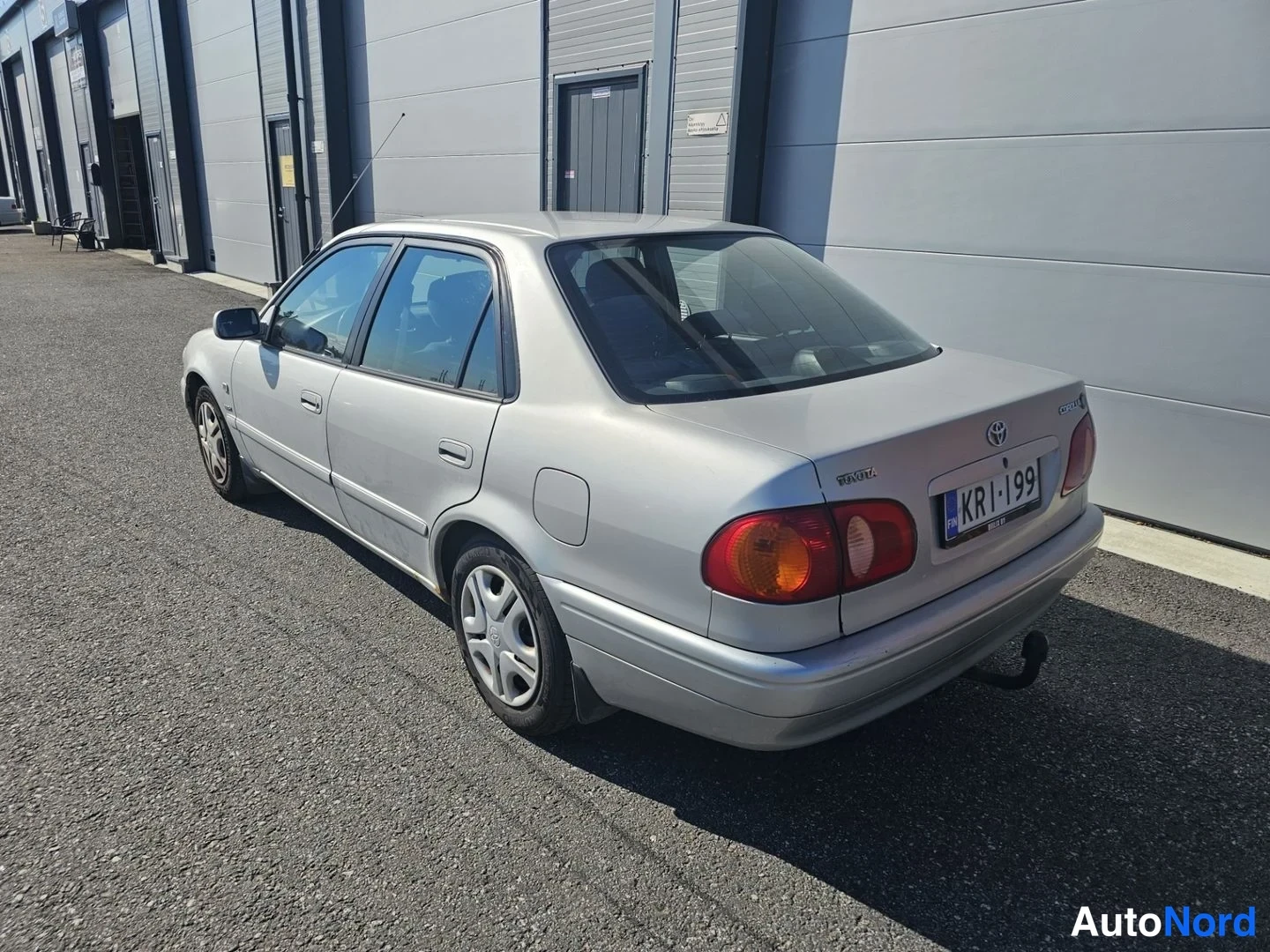Takaviisto: Hopeinen Toyota Corolla -sedan kuvattuna takavasemmalta päin; rekisterikilpi KR-199 luettavissa, takaosa ja vasen kylki näkyvissä.