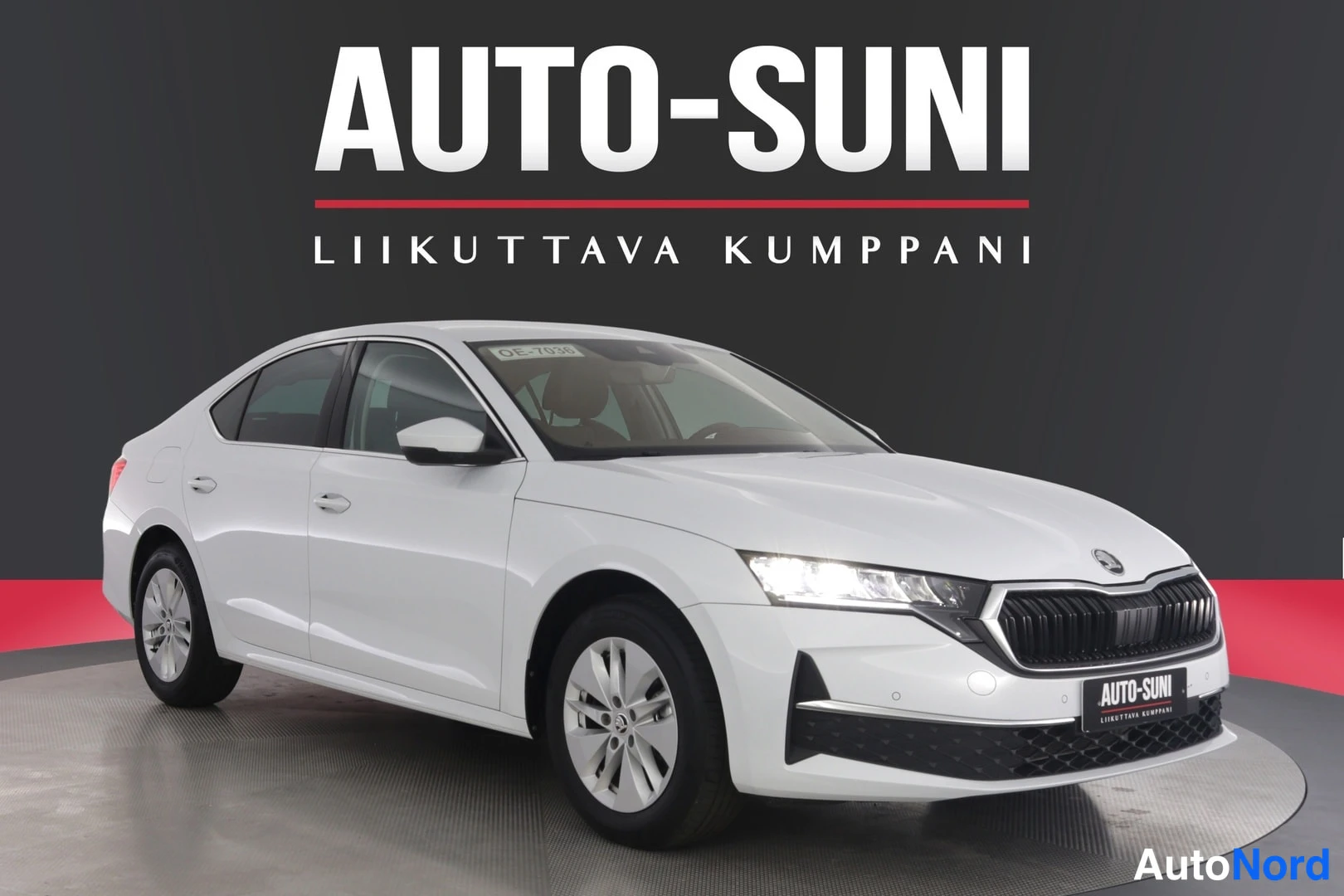 Etuviisto, nokka oikealle: Valkoinen Skoda Octavia -sedan etuosa kolmannelta kulmalta, etusuoja ja kylki näkyvät studiotaustaa vasten.