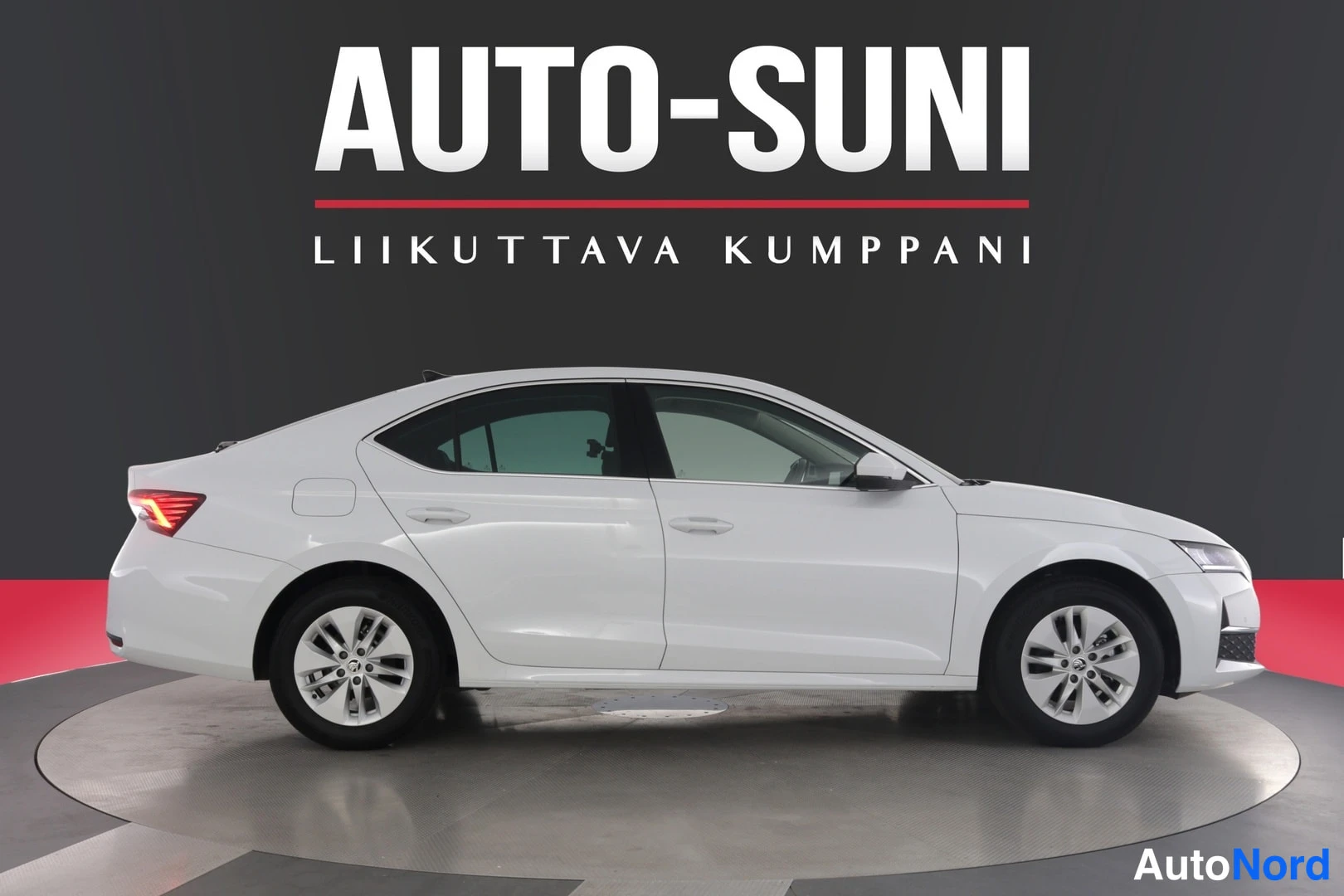 Sivulta: Valkoisen sedan-auton oikea kylki täydessä profiilissa studiovaaleaa harmaata taustaa vasten.