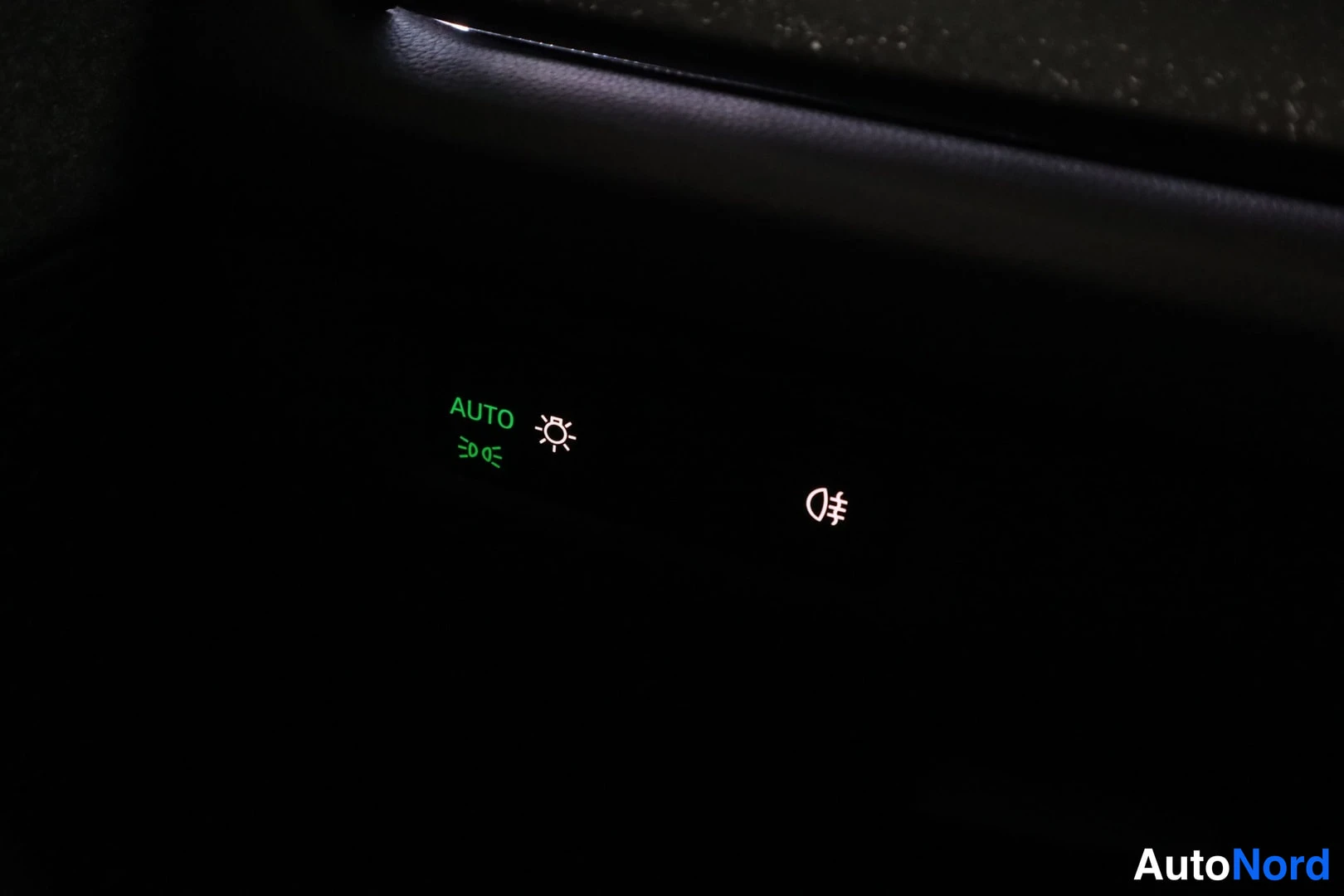 Muu: Valokytkimen AUTO-merkinnän ja sumuvalojen symbolin lähikuva pimeässä kojelaudassa.