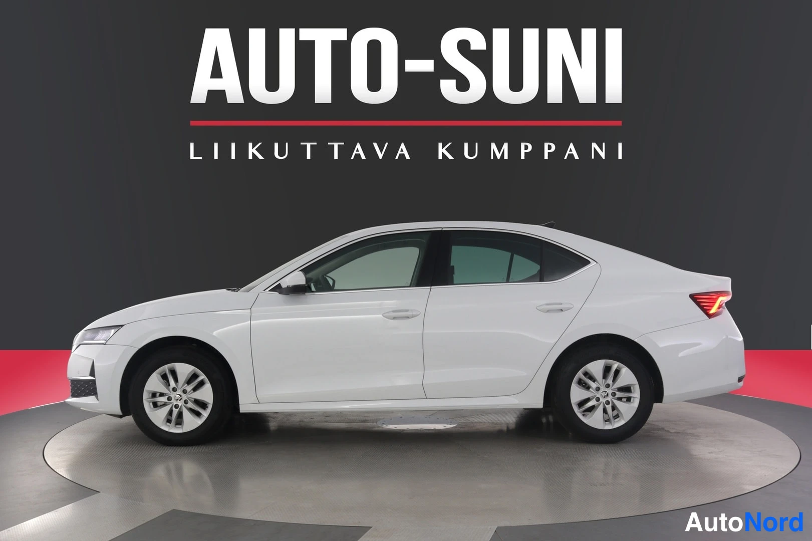 Sivulta: Valkoinen sedan-mallinen henkilöauto sivulta kuvattuna studiotaustaa vasten.