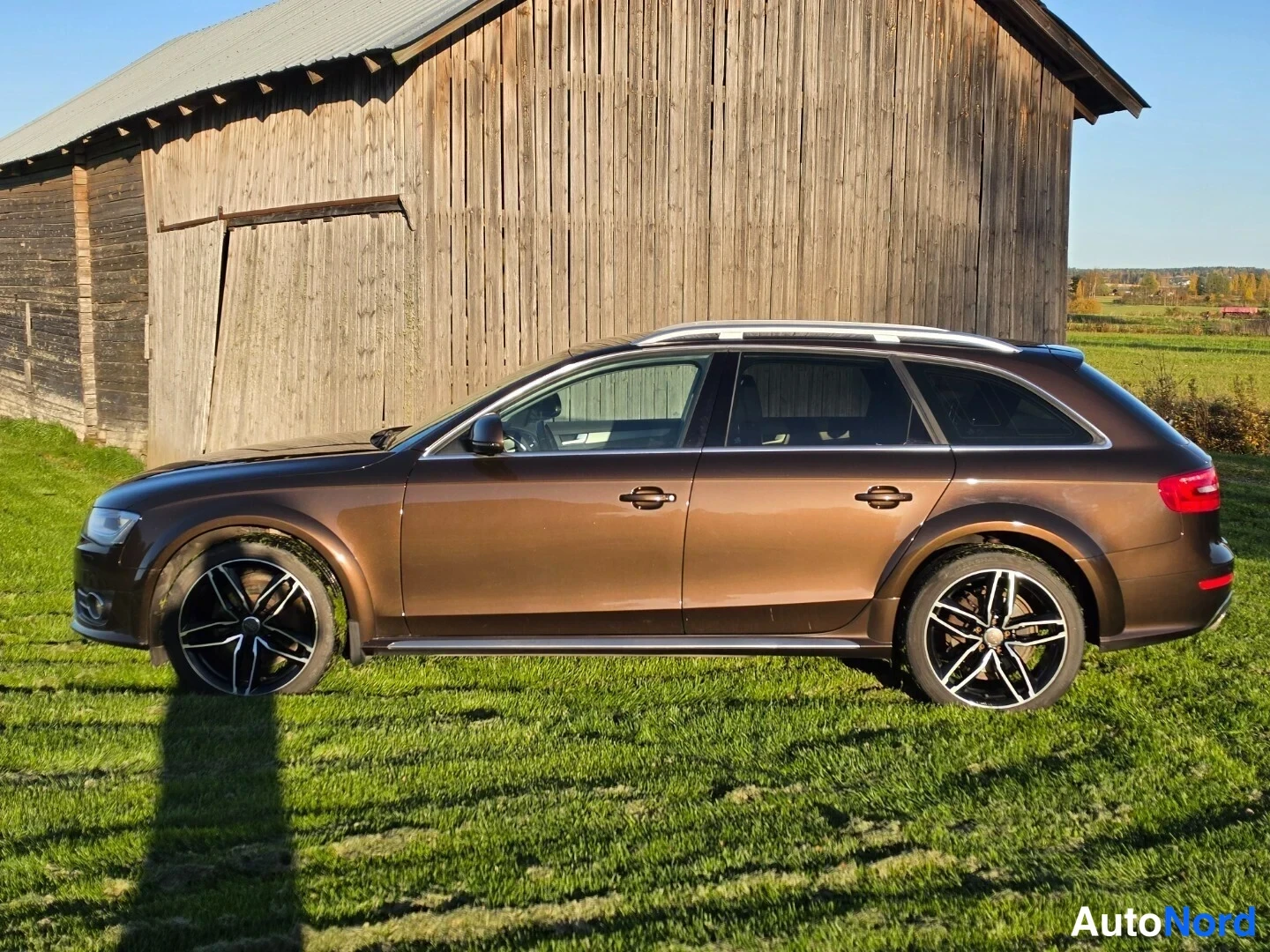 Sivulta: Puoli sivunäkökulma ruskeaan metalliväriseen Audi Allroad Wagon -autoon. Kattoon asennettu valkokultainen kattoikkuna ja takakulmassa punaisia hehkuaajuja.