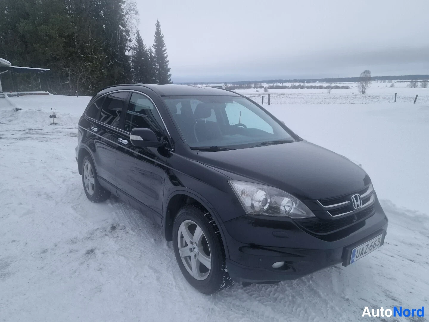 Etuviisto, nokka oikealle: Mustan Honda CR-V:n etänurkkakuva oikeasta edestä lumisessa ympäristössä, rekisterikilpi näkyvissä.
