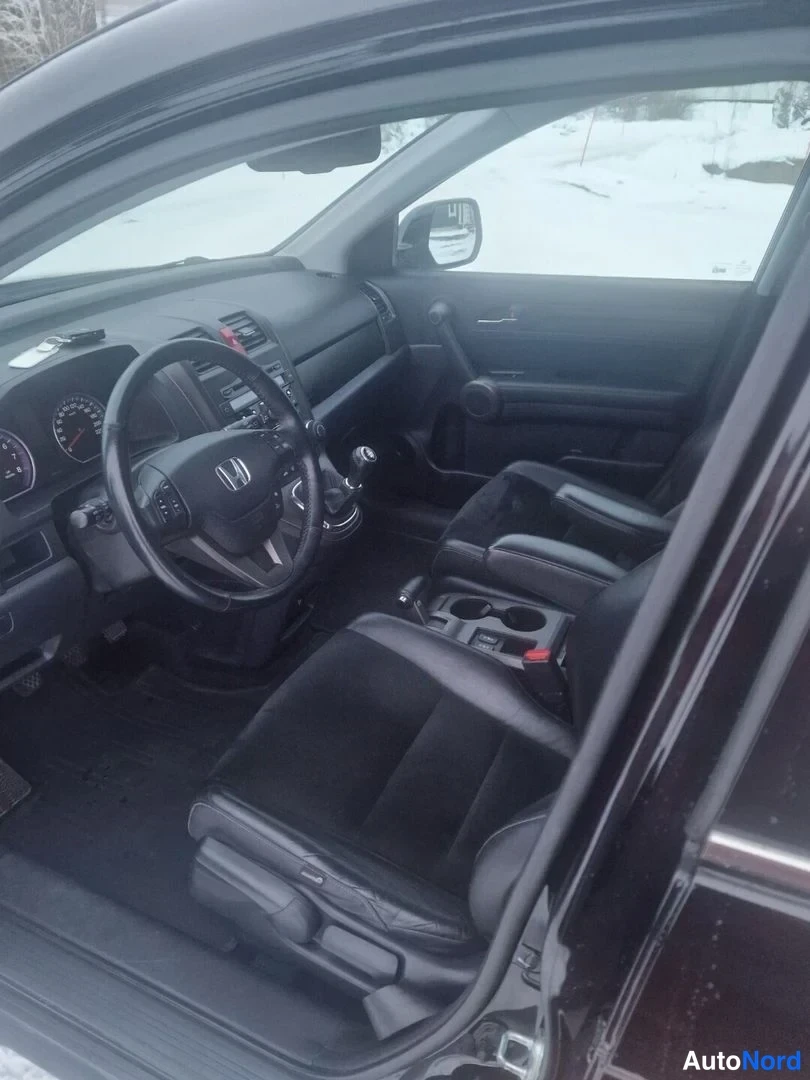 Muu: Honda CR-V:n etuistuin ja kojelauta oven avaamalta, ohjauspyörä ja keskikonsoli näkyvät.