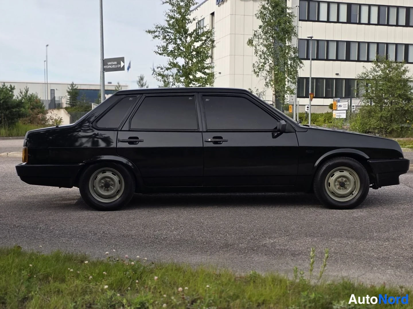 Etuviisto, nokka oikealle: Musta sedan-sedan sivulta, hieman keulaa oikealla ja perää vasemmalla näkyvissä.
