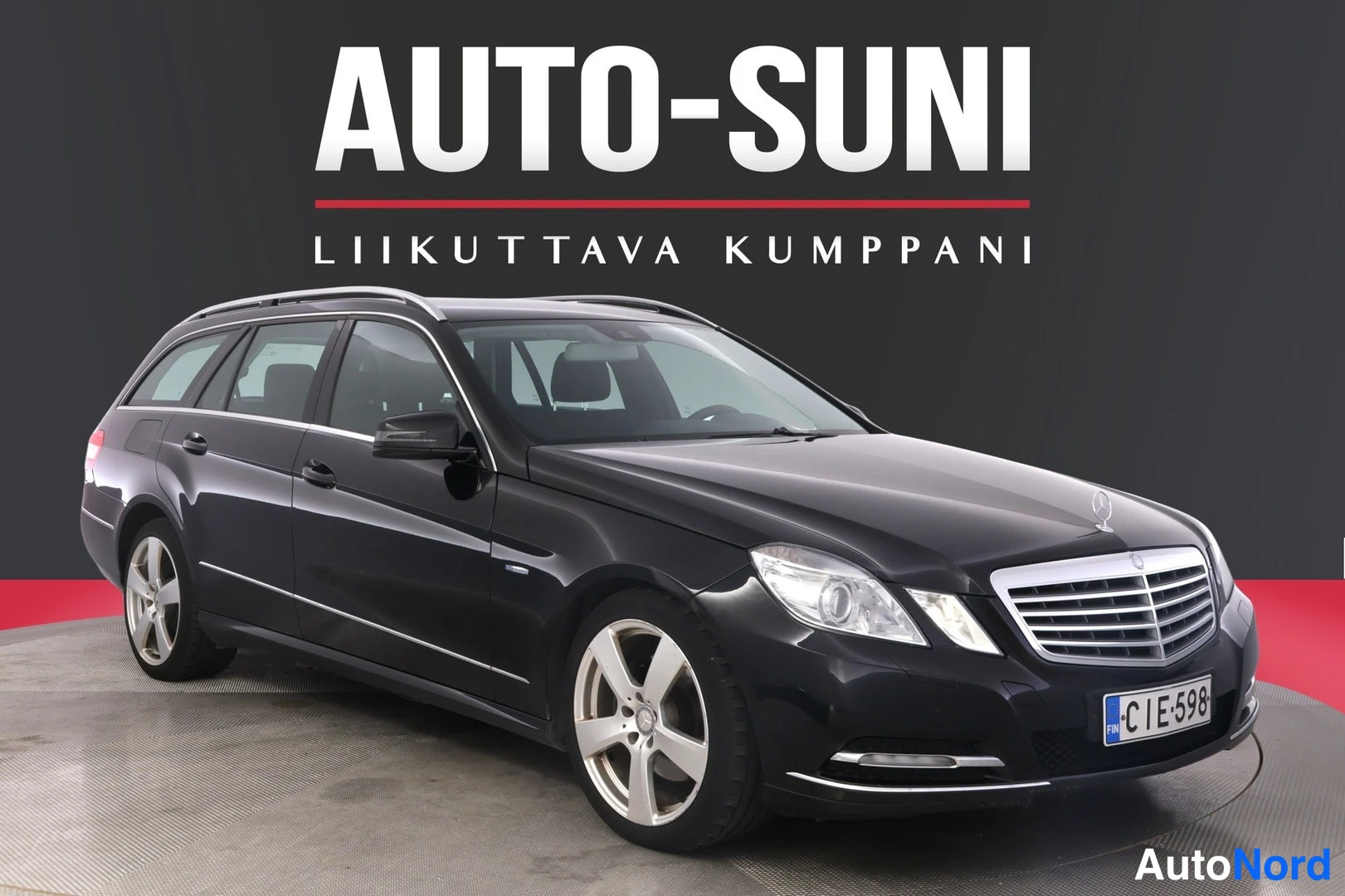 Etuviisto, nokka oikealle: Musta Mercedes-Benz E -farmari etuviistöstä oikealta, kattokaiteet näkyvät.