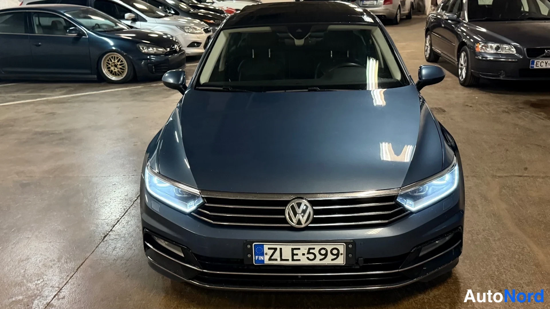 Edestä: Tummansininen Volkswagen Passat suoraan edestä, rekisteri, LED-päiväajovalot päällä.
