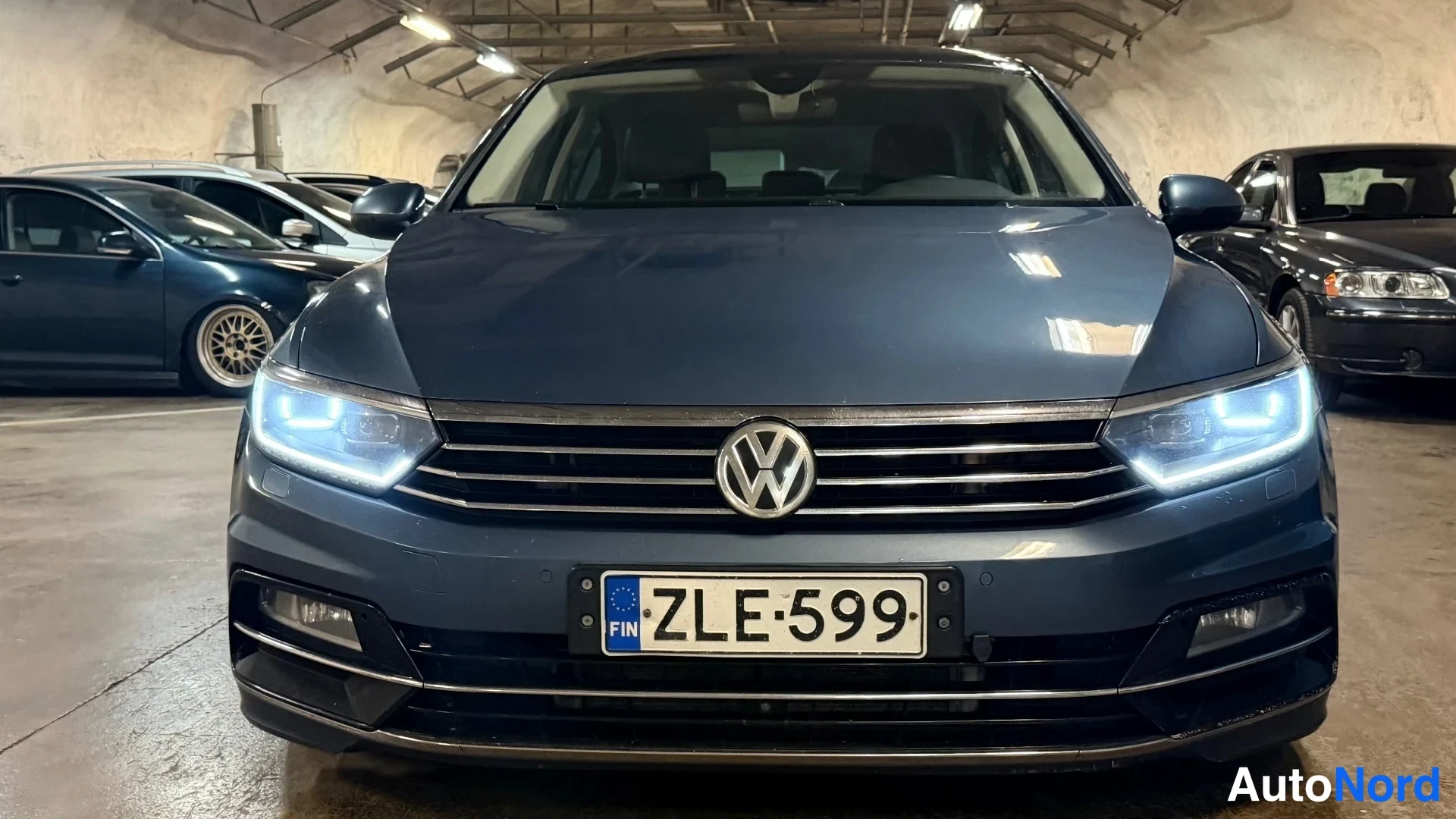 Edestä: Tummansininen Volkswagen Passat suoraan edestä, LED-etuvalot päällä, rekisteri.