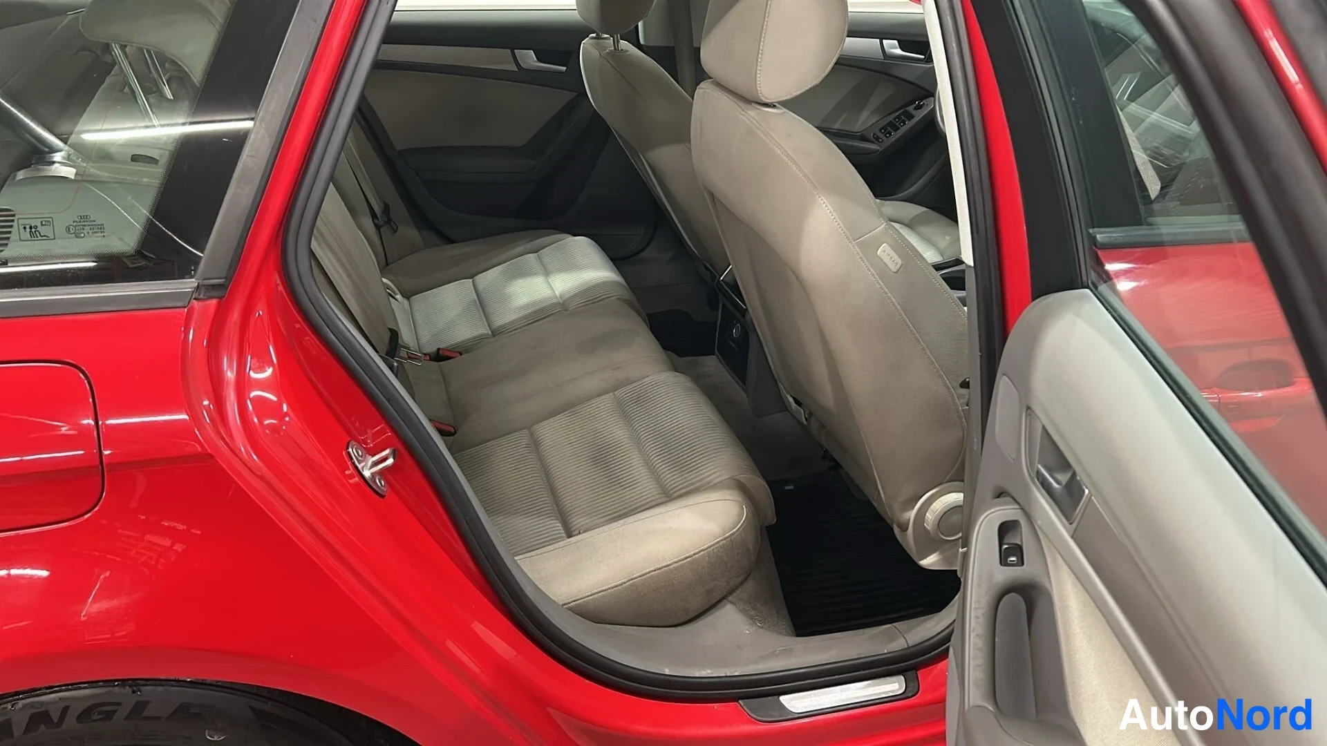 Sivulta: Avaamaton takiovi paljastaa beige-rippikankaalla verhatut takapenkit ja etumatkan Audi A4 Avantissa; punainen koriajälki näkyy oviaukon reunoilla.