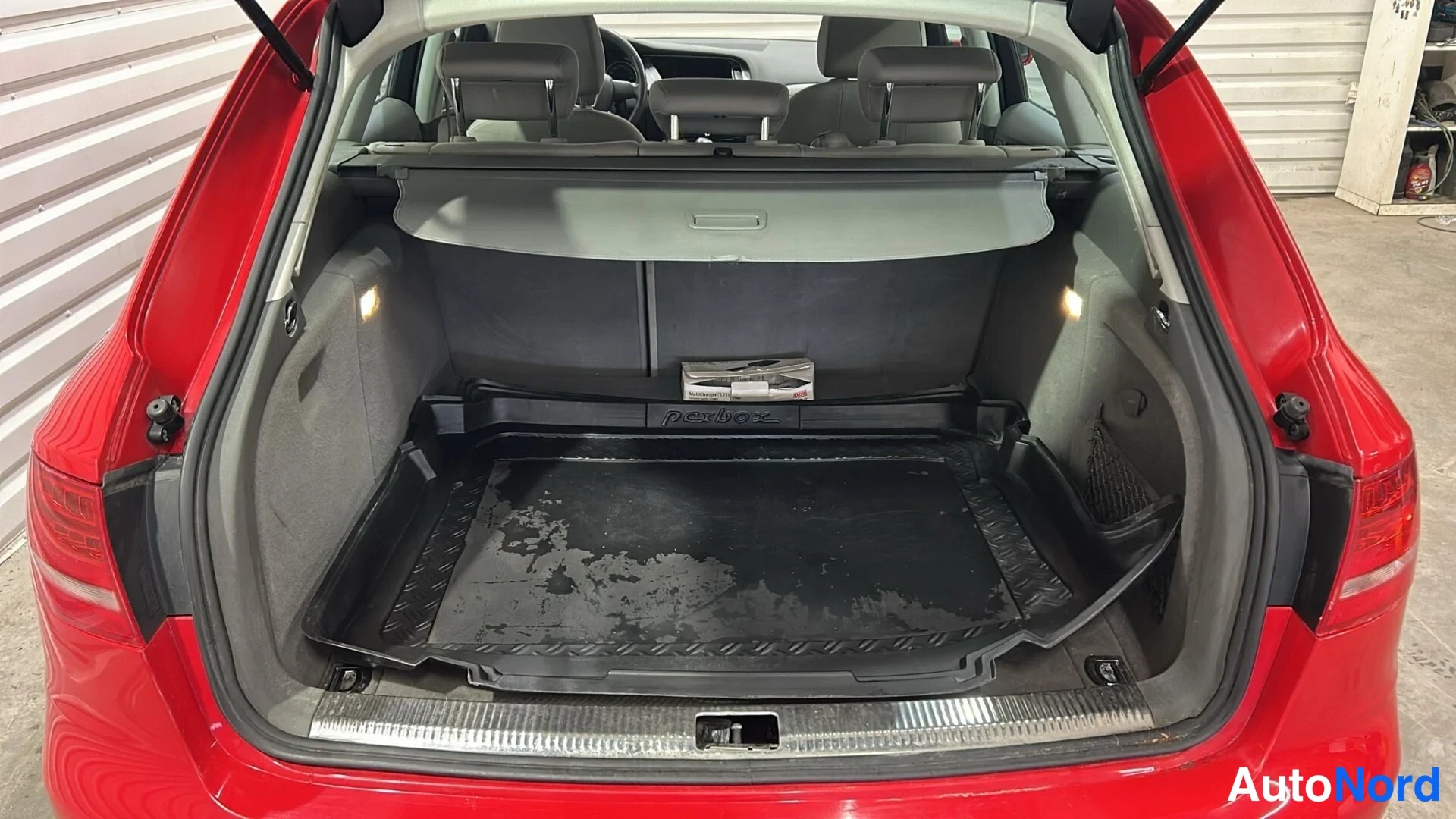 Takaa: Avoimella takaluukulla esillä oleva tavaratila suoralla lautalattialla, ilmastointiverho ja pörbox-laatikko; auton takapää on punainen.