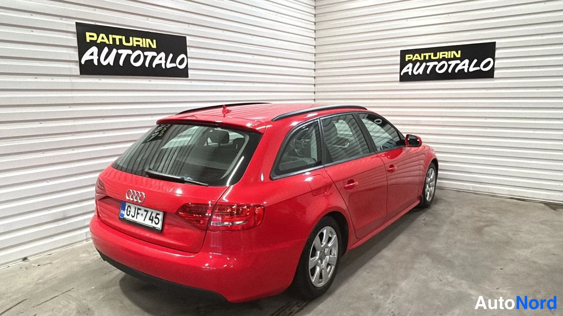 Takaviisto: Punainen farmariauto takakulmasta hallissa, perä ja oikea kylki näkyvissä.