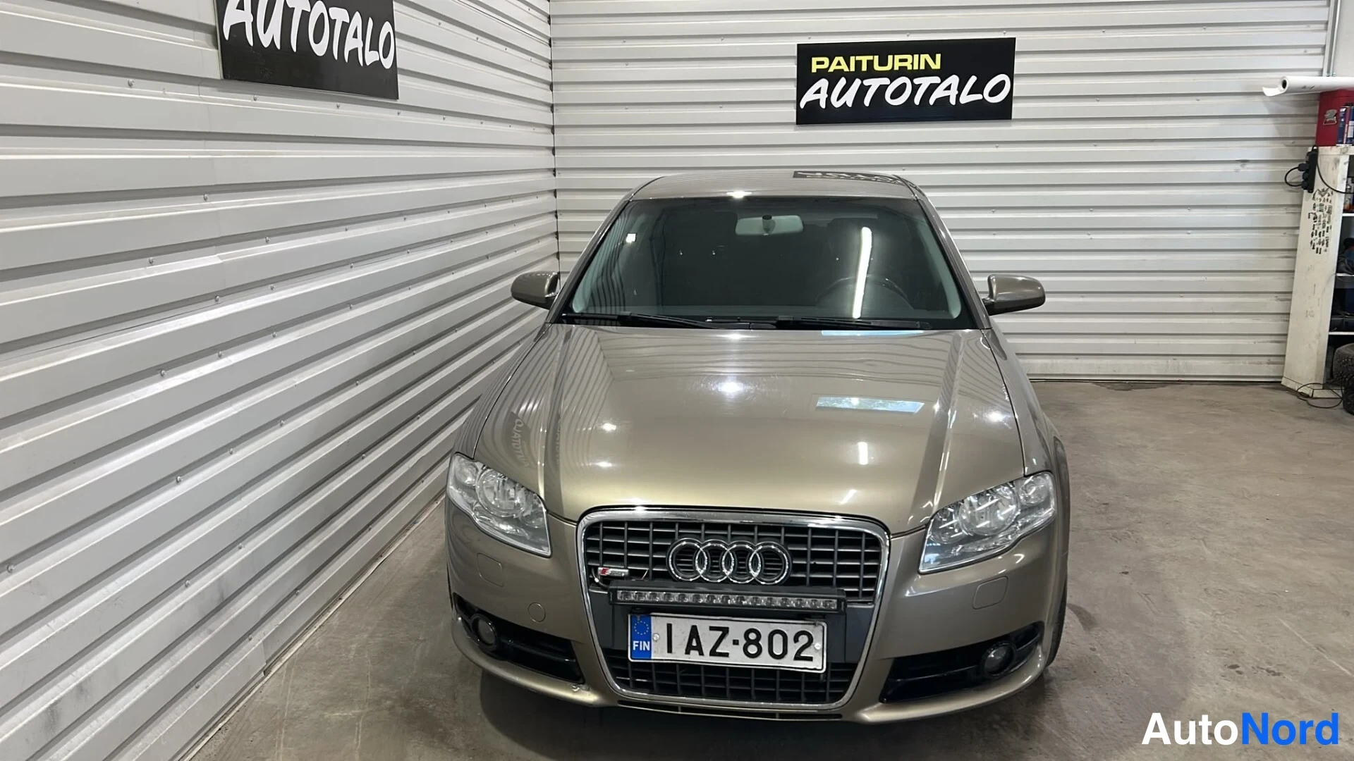 Edestä: Beige auton keula suoraan edestä kuvattuna; Audi-kyltti, ajovalot ja rekisterikilpi näkyvissä.