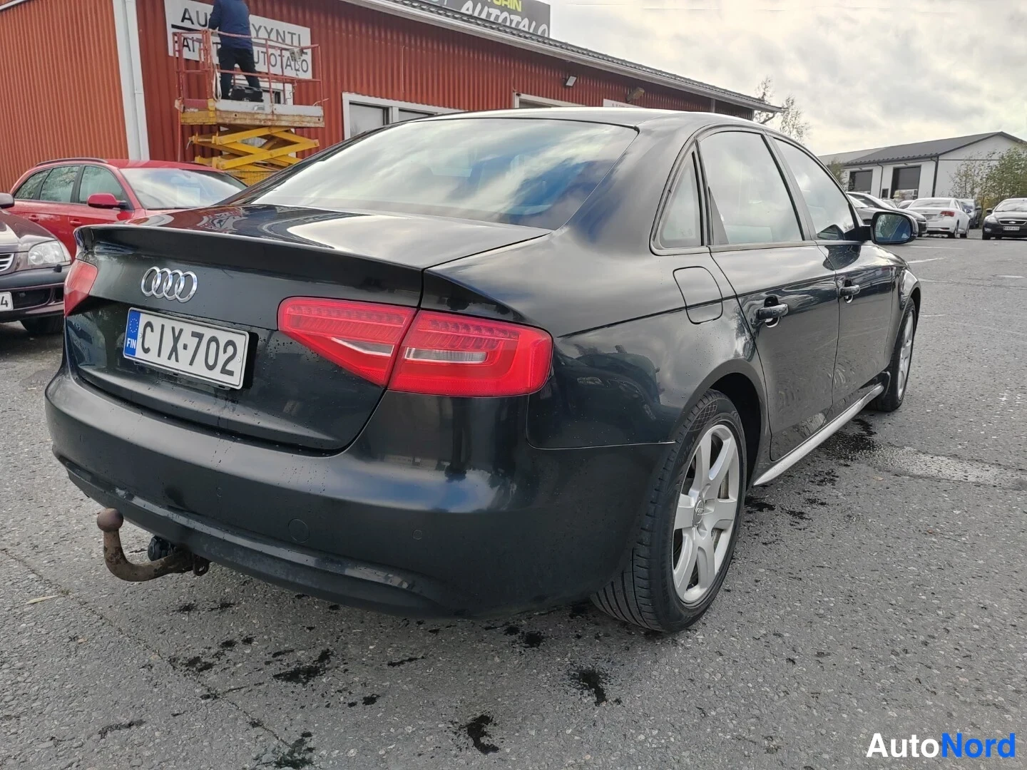Takaviisto: Tummansininen sedan kuvattu takakulmasta vasemmalta; takavalo, Audi-merkki, rekisteritunnus ja irrotettava vetoaisa tagilla näkyvät.