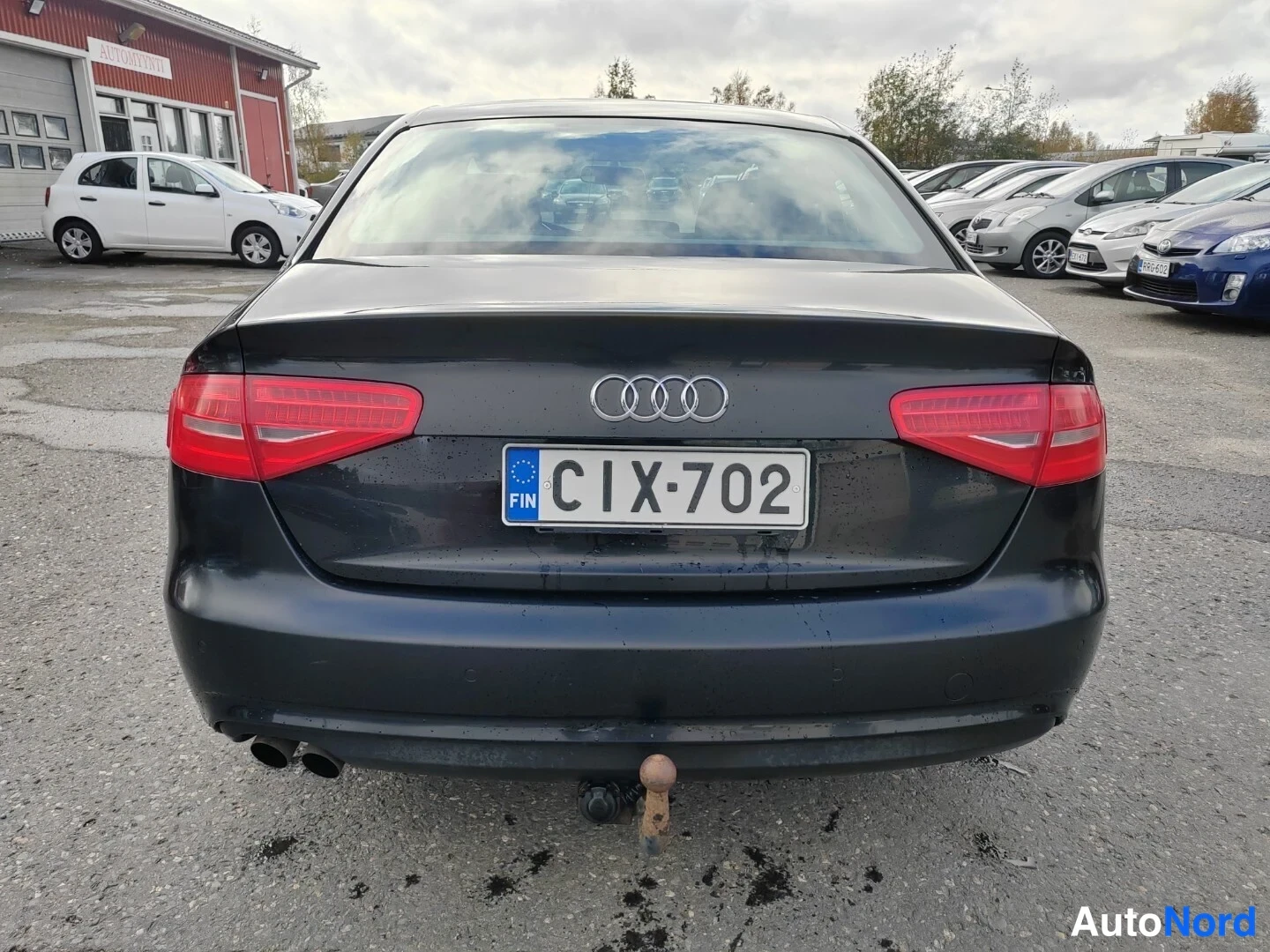 Takaa: Tummansininen sedan suoraan takaa; kaksi takavaloa, Audi-nelirengas, rekisterikilpi, kaksiosainen pakoputki ja vetokoukun kaula.