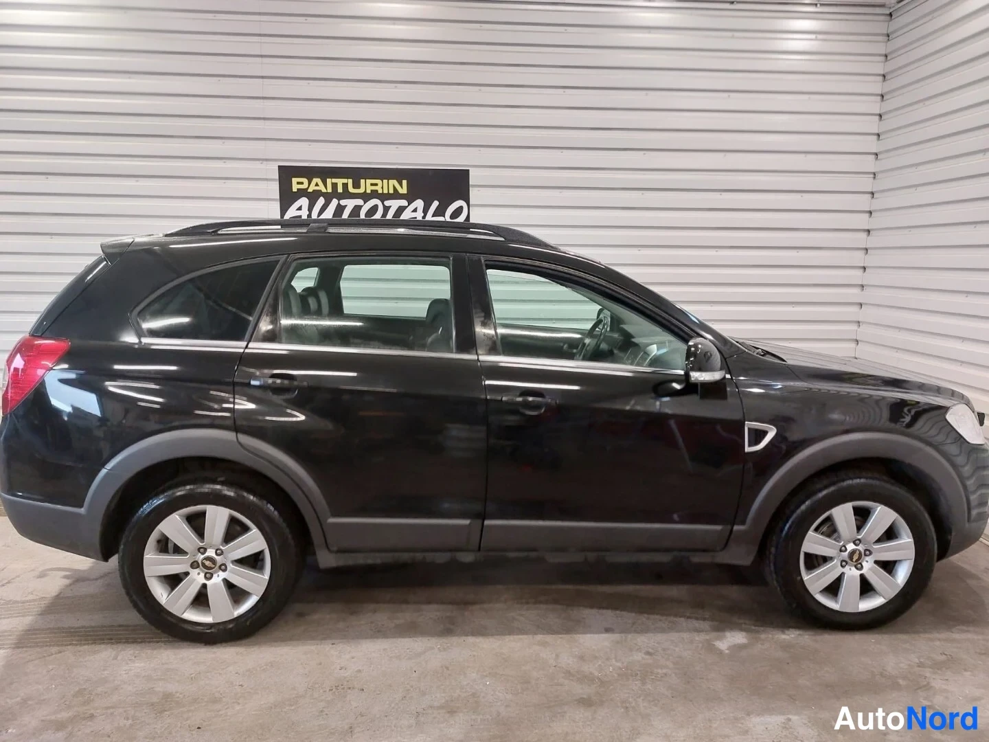 Sivulta: Musta Chevrolet Captiva -katuauton vasen sivunäkökulma sisätilassa. Kevyen metalliset vanteet ja katutelineet ovat selvästi nähtävissä.