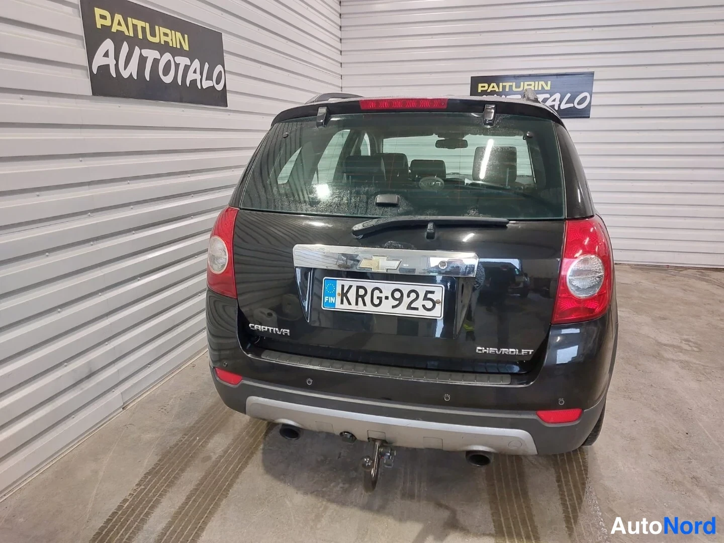 Takaa: Musta Chevrolet Captiva -katuauton taka-alaosa. Auto seisoo asennossa, jossa molemmat takavalot näkyvät täysin. Kiiltävä pinta ja heijastukset ovat selvät.