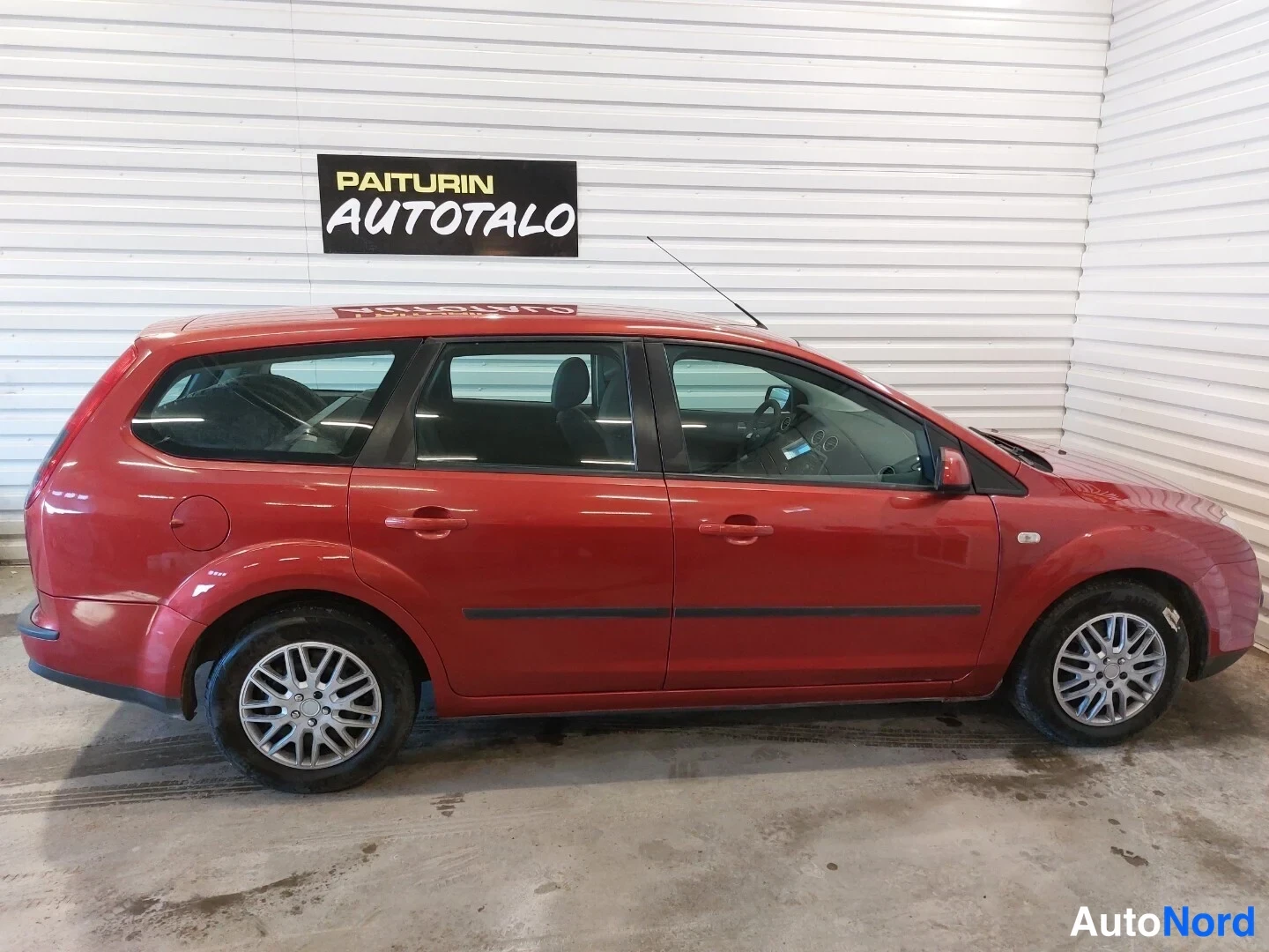 Sivulta: Punaisen Ford Focus -farmarin sivukuva vasemmalta kyljestä valkoisessa hallissa.